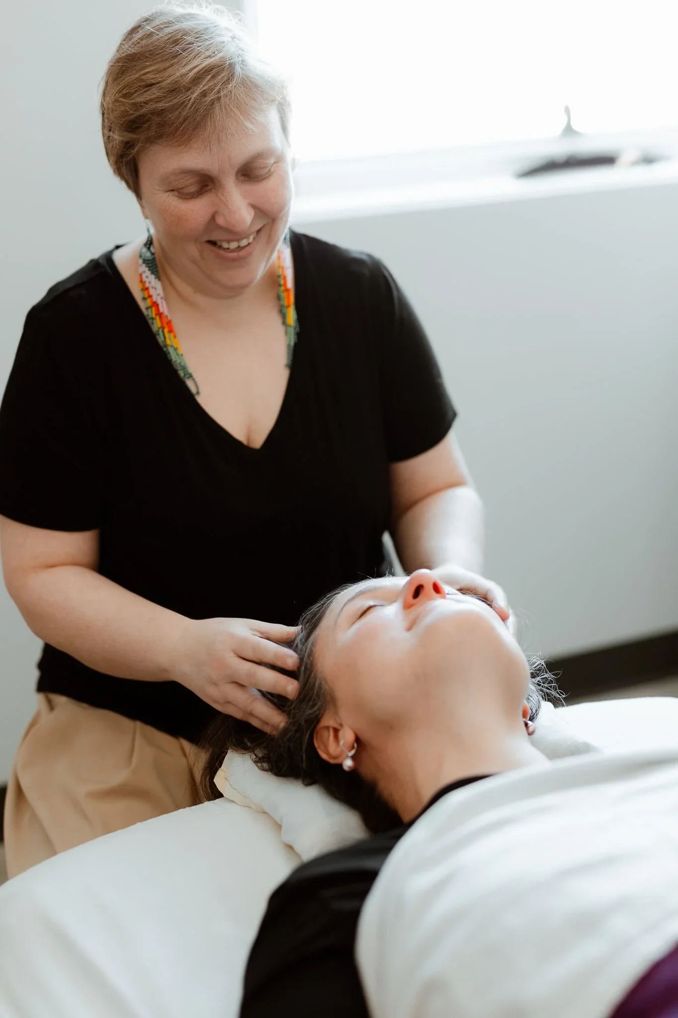 Une esthéticienne ou thérapeute effectue un soin de massage facial ou crânien à une cliente allongée.