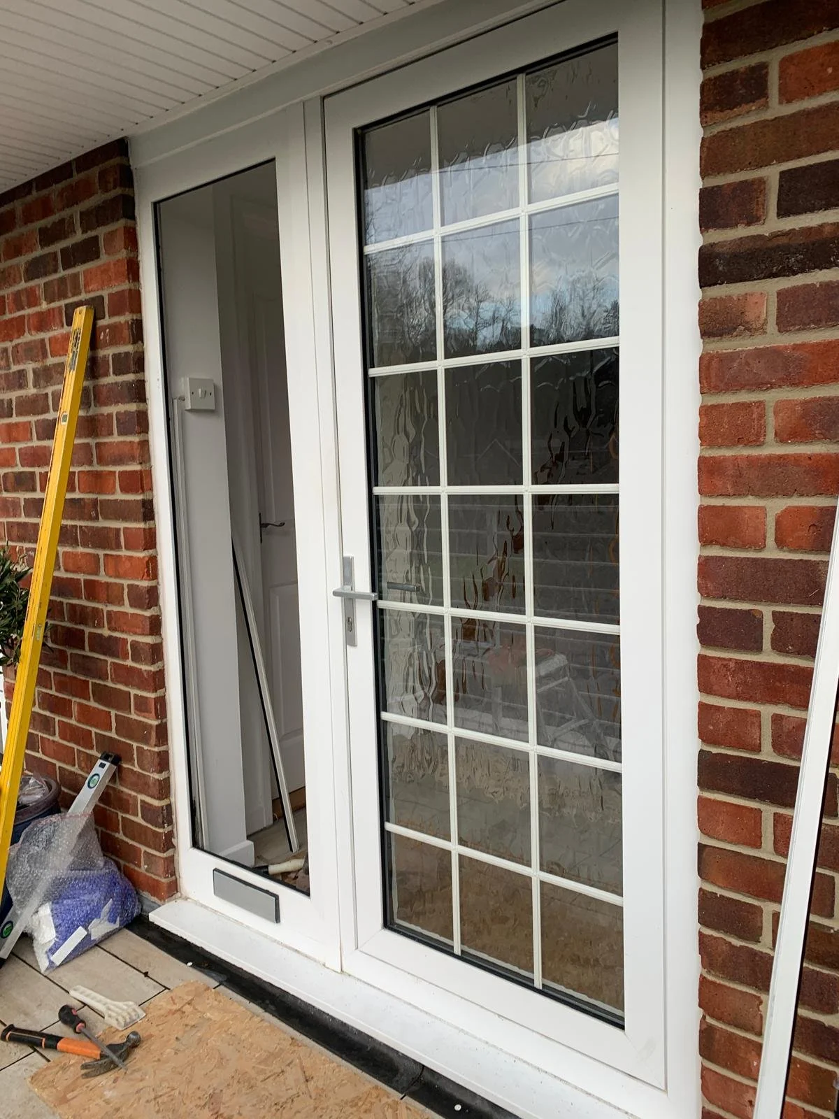 A new white sliding glass door being installed on a brick house exterior, with tools and construction materials nearby.