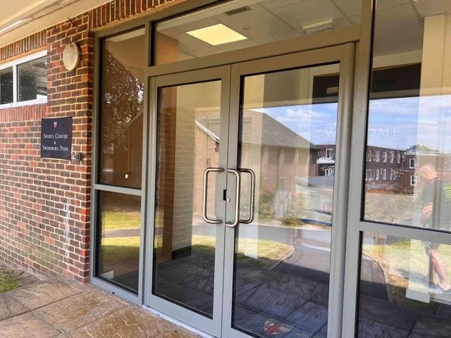 Double glass doors with metal handles leading into a building with a brick exterior and large windows.