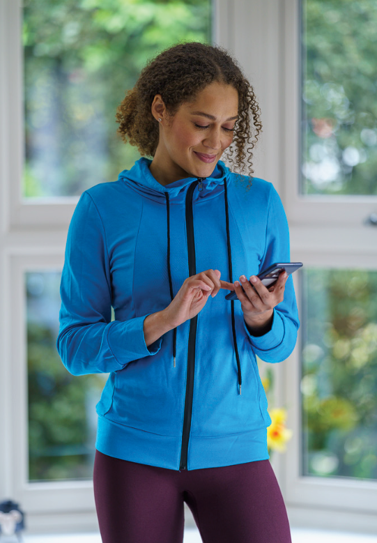 Woman in blue athletic hoodie looking at her smartphone indoors.