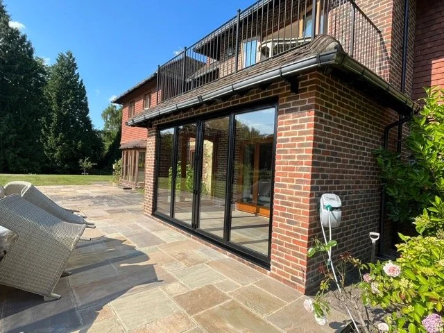 Back patio area with outdoor seating and glass sliding doors leading into a brick house with a balcony.