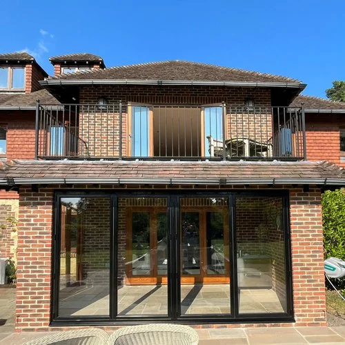 Bricked house with a glass enclosed patio on the ground floor and a balcony with a metal railing on the upper floor, under a blue sky.