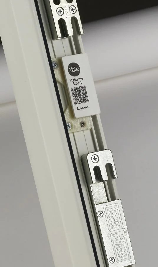 Close-up of a white mechanical support track with metal brackets and a Yale smart tag with QR code attached to the side.