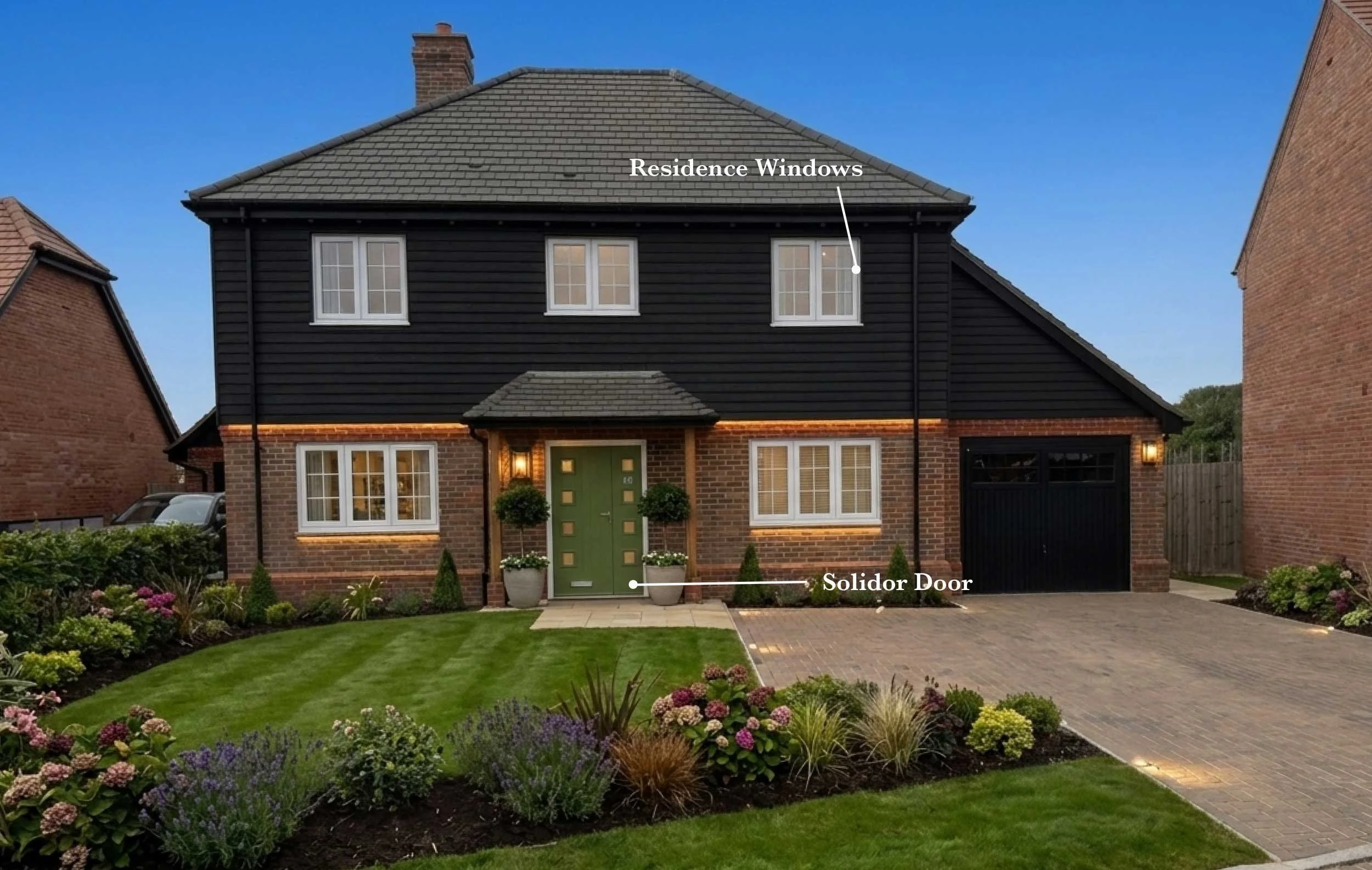 Front view of a modern two-story house with a brick and black siding exterior, a green front door, and three large residential windows. Well-maintained front yard with green grass, flower beds, and small bushes, and a paved driveway and walkway.