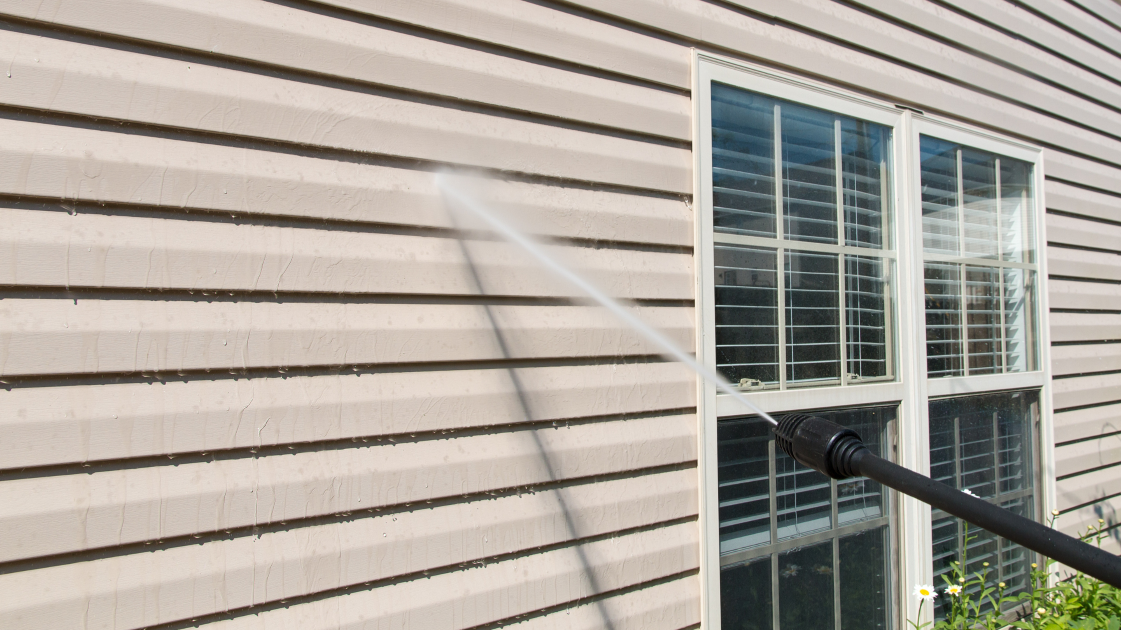 A person cleaning a siding with pressure wash wand.