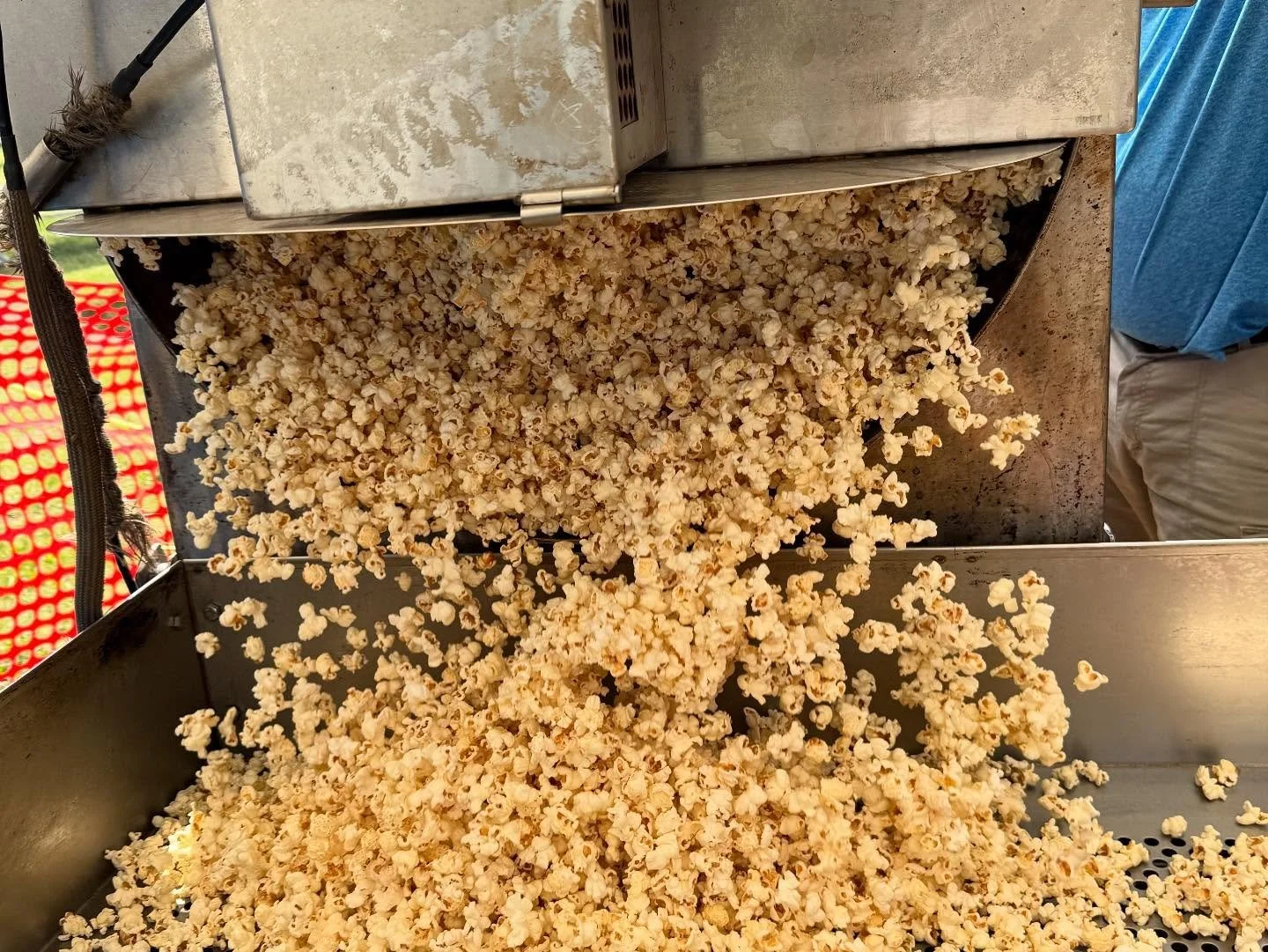 Freshly popped popcorn falling into a metal container at a popcorn stand.