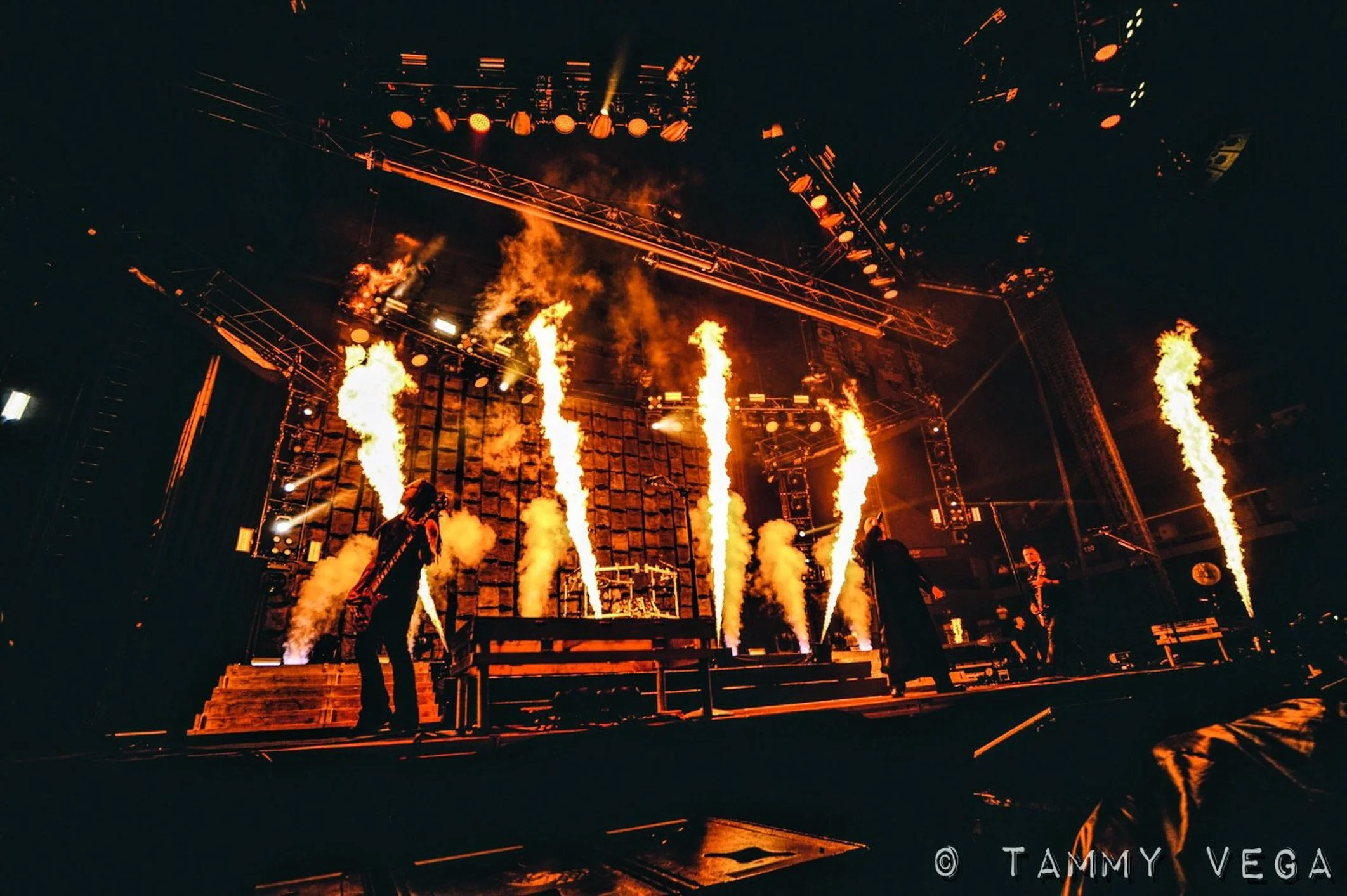 Stage with pyrotechnics and lighting during a concert or event, performers visible on stage with flames shooting upward.