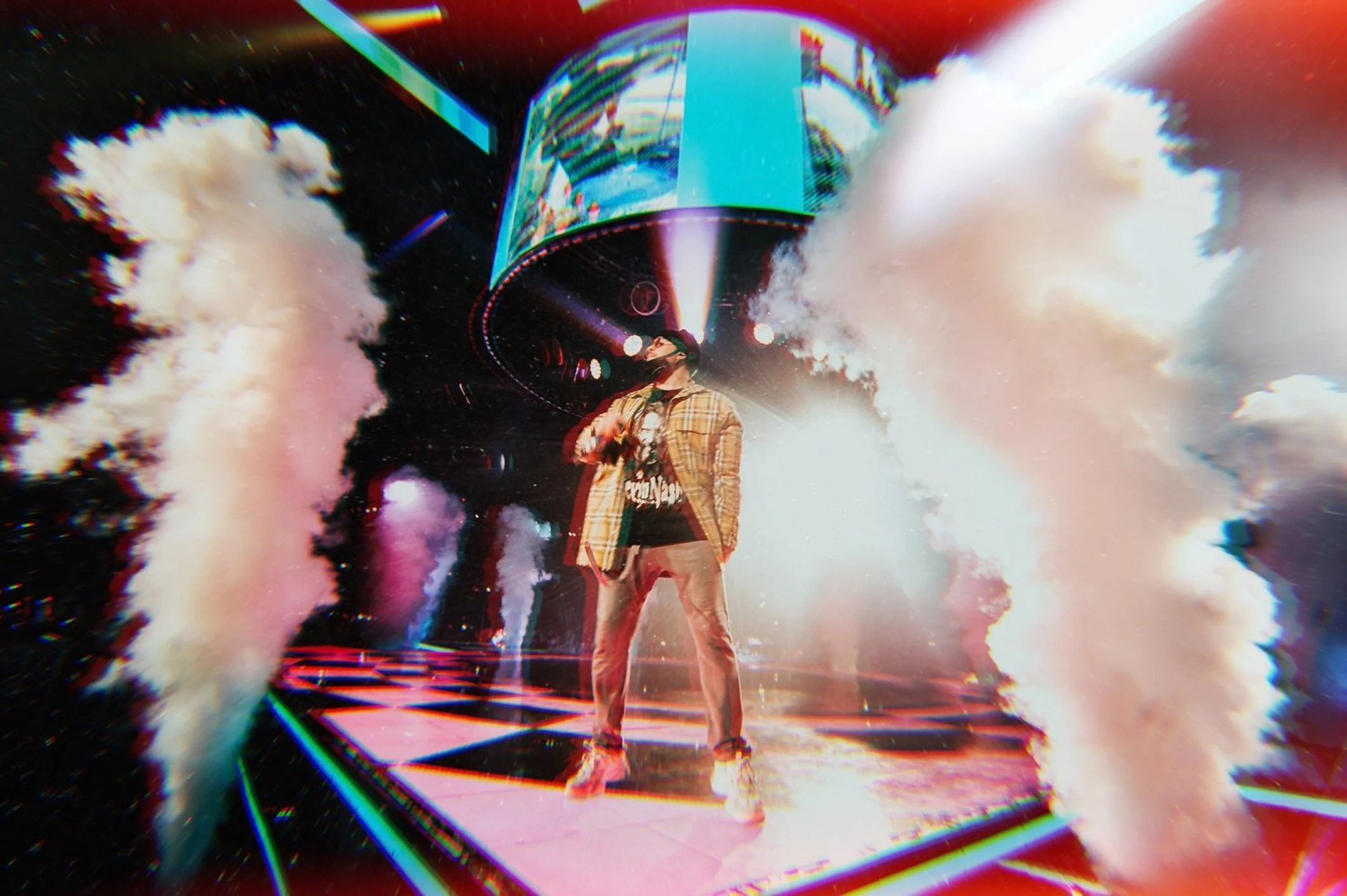 A woman standing in front of a large digital screen with colorful visual effects and clouds of smoke around her, creating a futuristic or cyberpunk aesthetic.