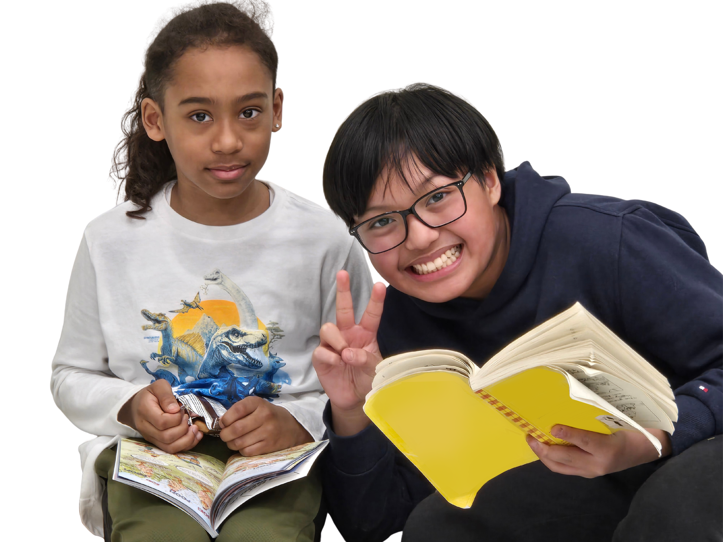 Two children sitting together, one reading a book and the other holding a snack, both smiling and making peace signs.