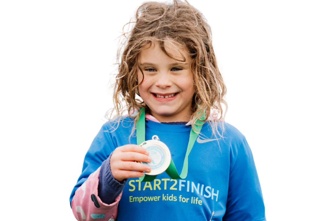 A young girl smiling and holding a medal at a kids' race event, wearing a blue START2FINISH shirt and a medal around her neck.