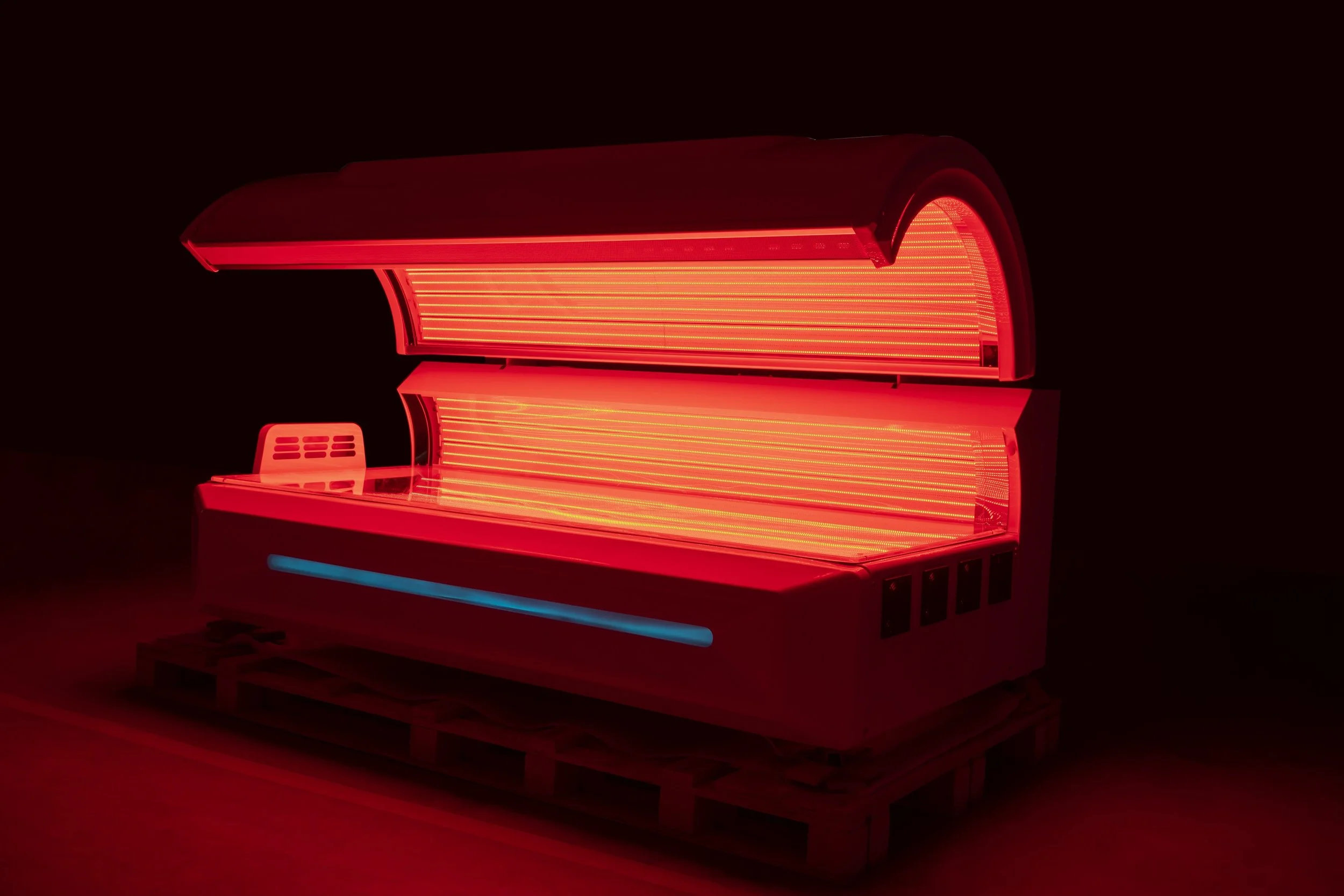A tanning bed with bright red UV lights on a dark background.