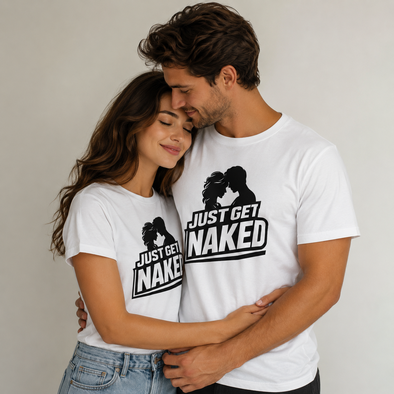 A young couple wearing matching white T-shirts with the phrase 'Just Get Naked' and a silhouette of a man and woman inches apart, smiling and embracing each other lovingly.