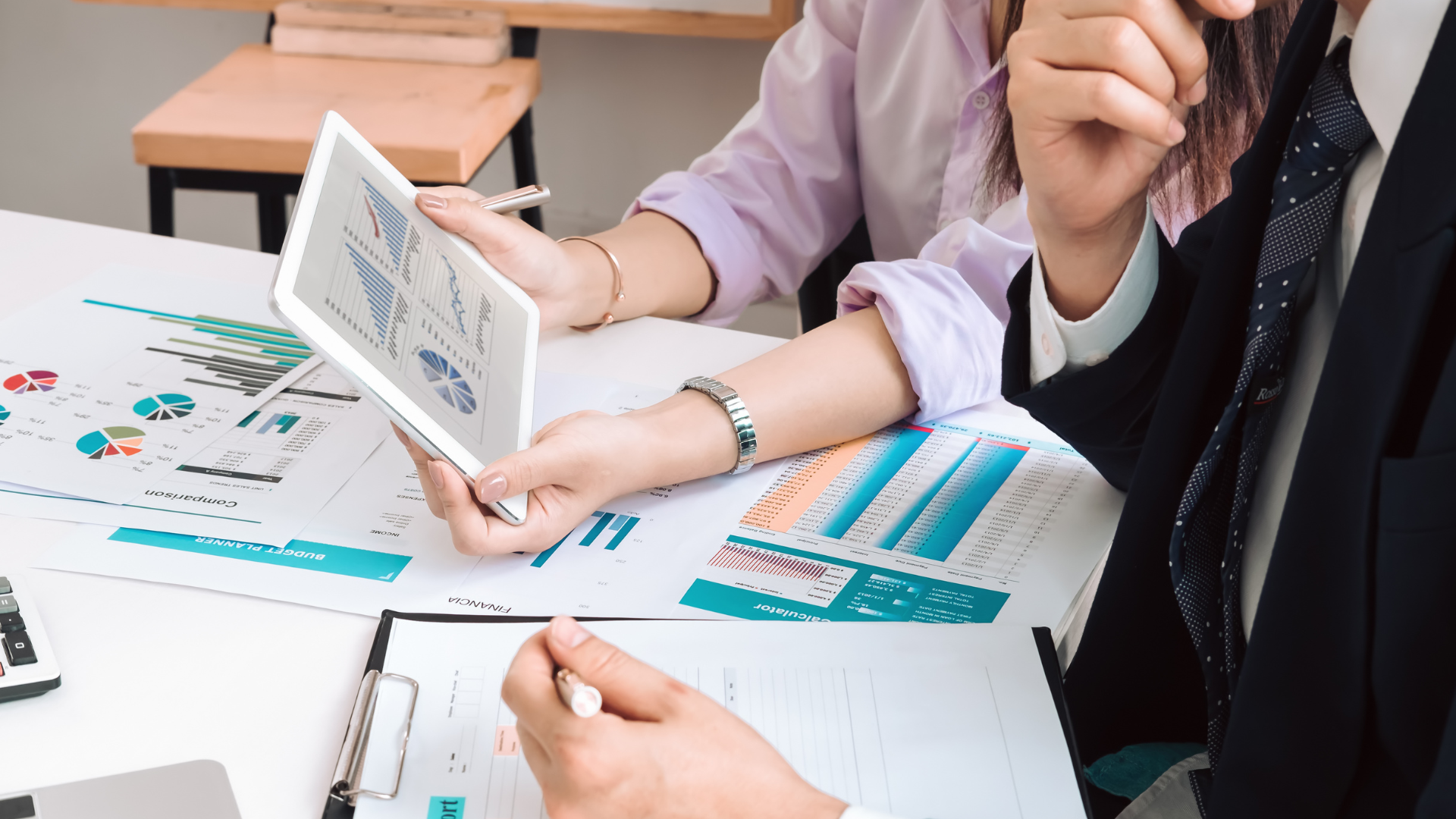 Two professionals reviewing financial graphs and charts with a tablet and papers on a conference table.