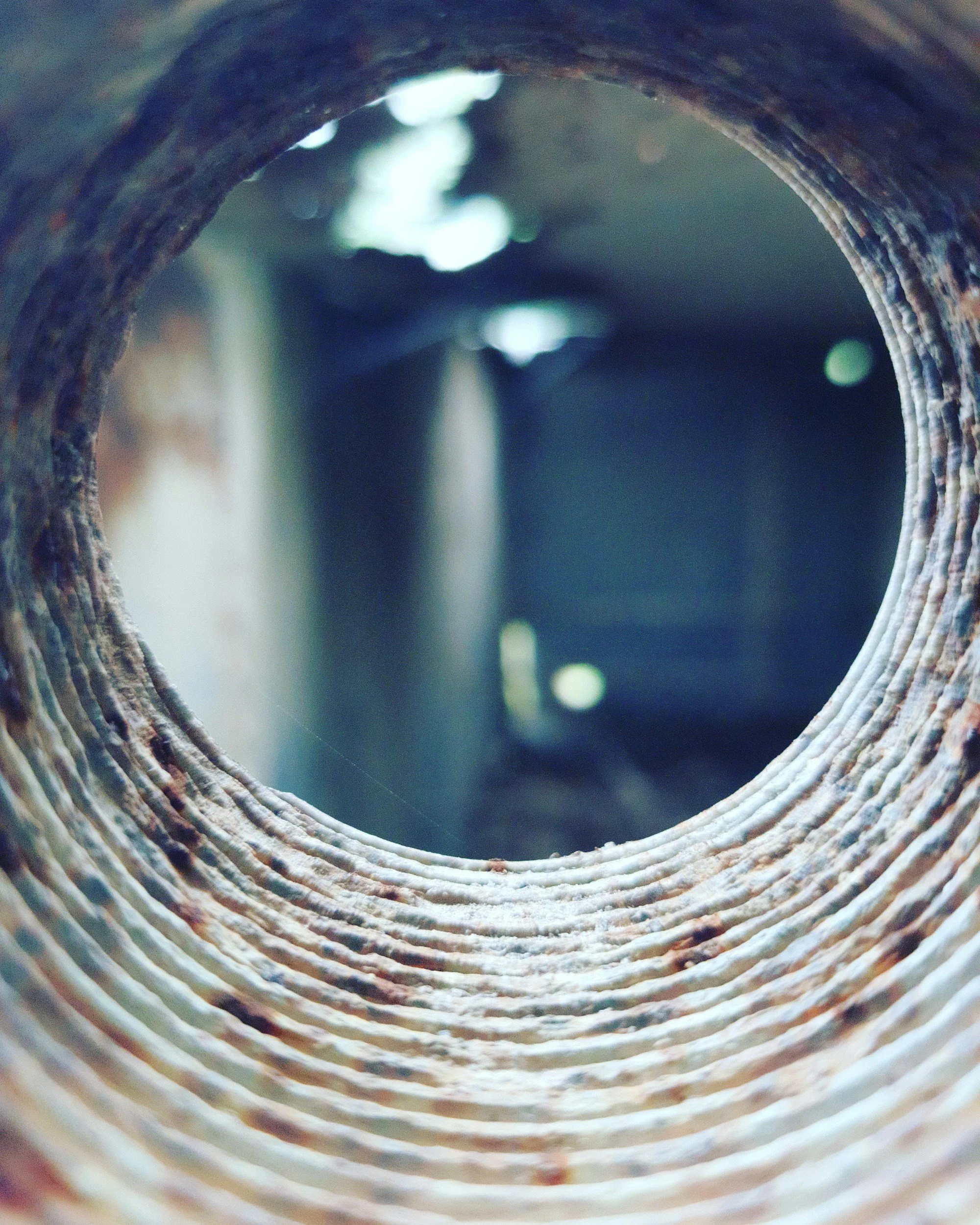 Close-up of a metallic pipe interior with ridges and rust, and a blurred background of light and dark colors.