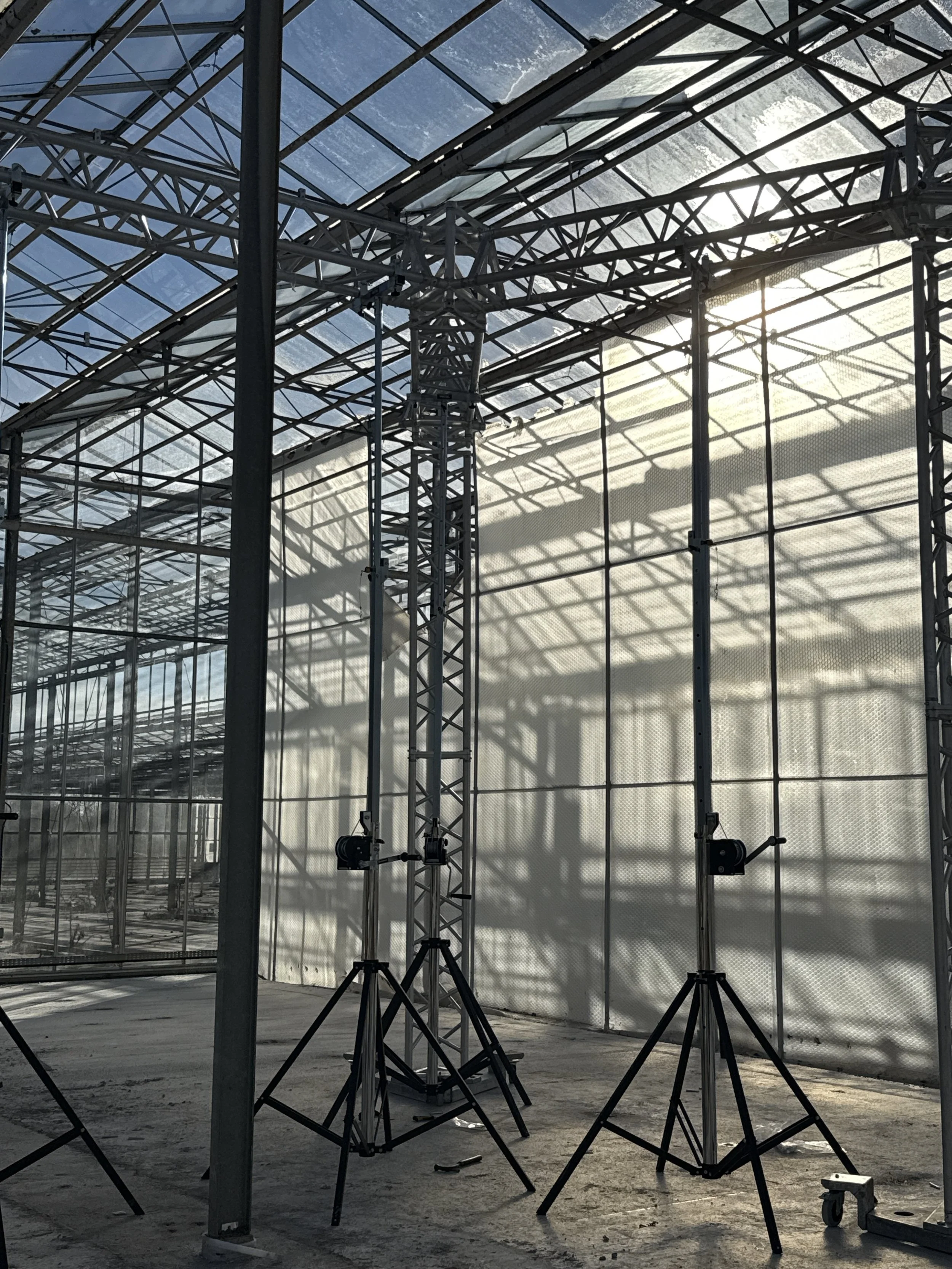 Construction site with metal scaffolding and support beams inside a partially built structure, with sunlight shining through the roof.