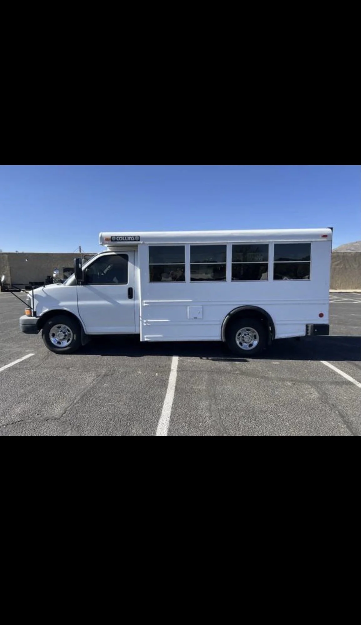 A white shuttle bus parked in an empty parking lot under a clear blue sky.
