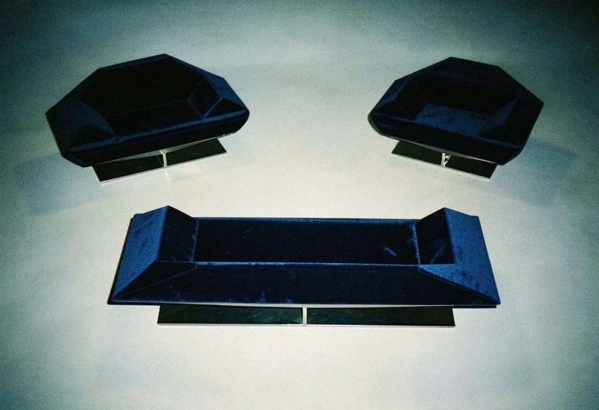 Un mobilier de salon composé d'un canapé et de deux fauteuils, tous en velours bleu foncé, exposés dans une pièce avec un éclairage tamisé.