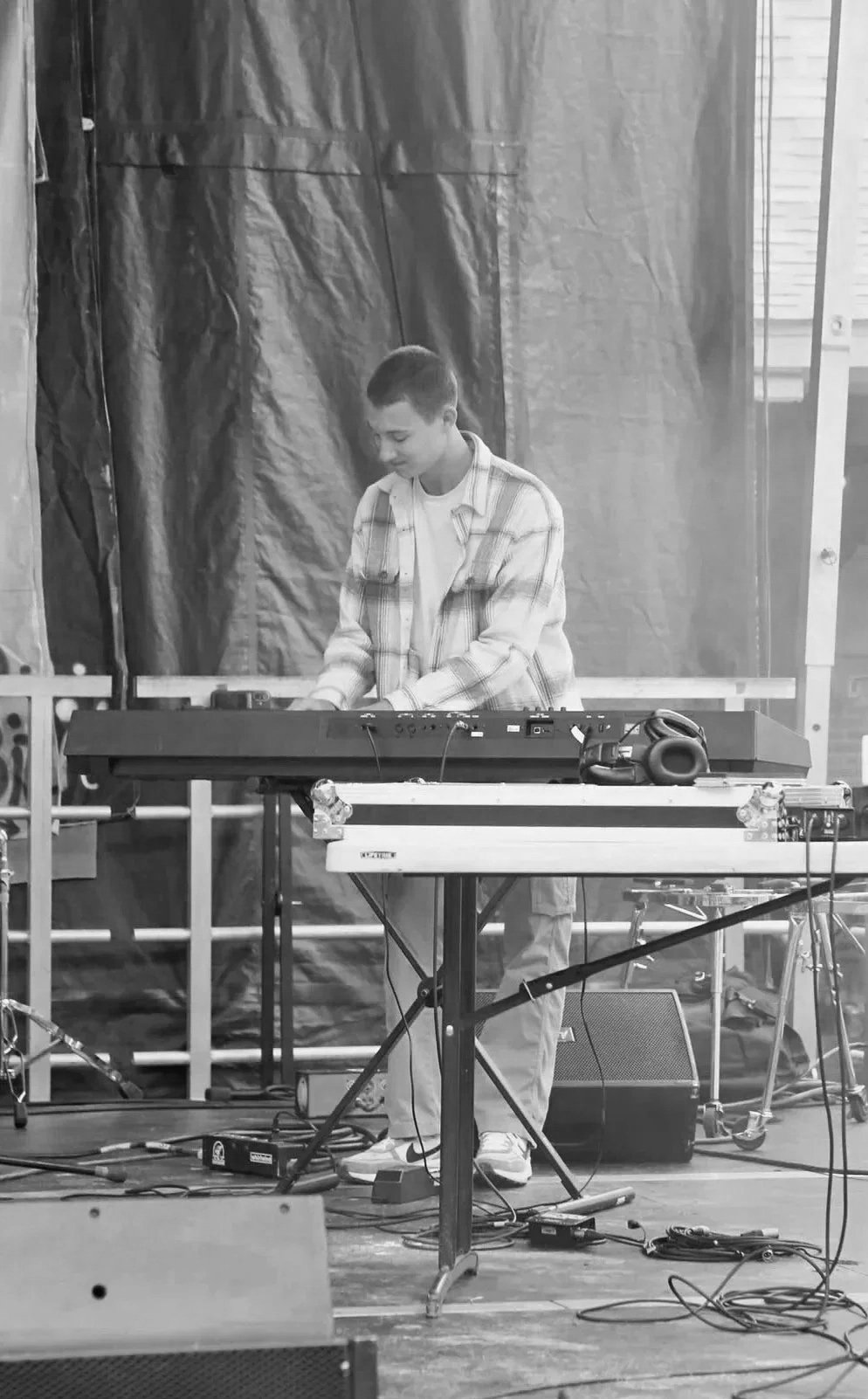 Isaiah Vinay playing keys on stage during a live music performance, surrounded by cables and music equipment.