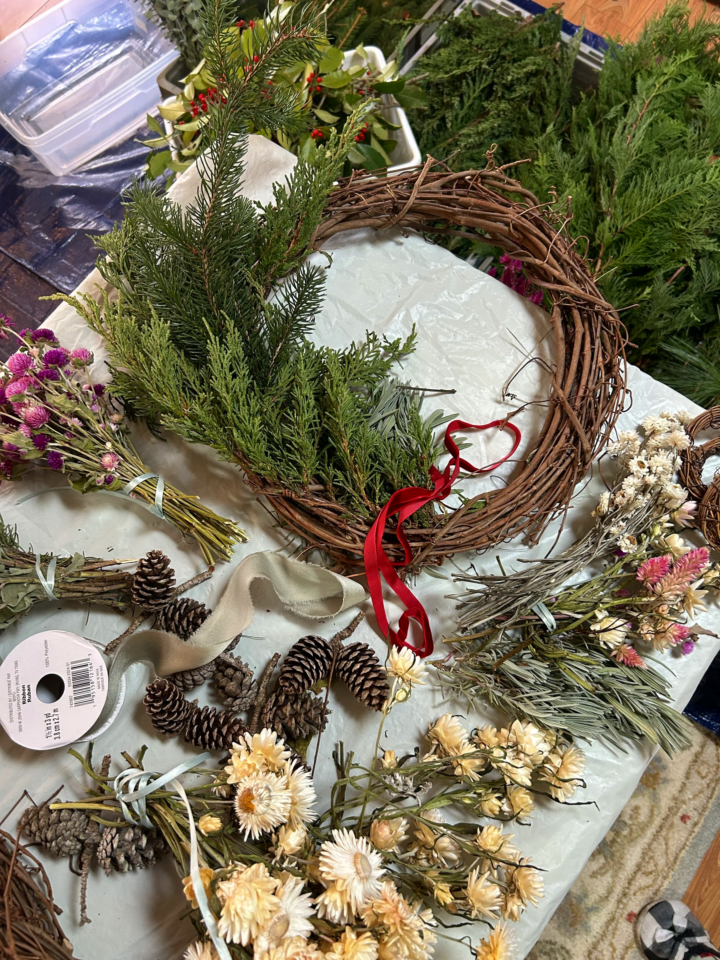 Collection of holiday decorations including a grapevine wreath, pinecones, dried flowers, and various greenery on a table.