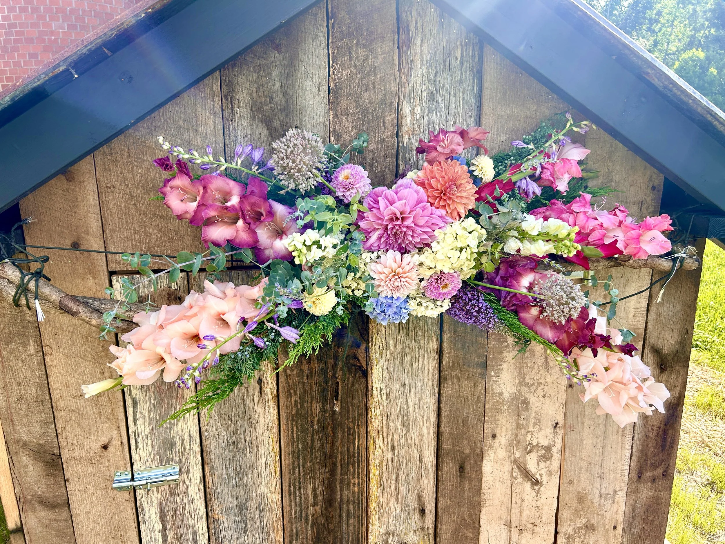 Colorful bouquet of flowers including pink dahlias, purple lisianthus, and other various flowers, arranged on a rustic wooden surface.