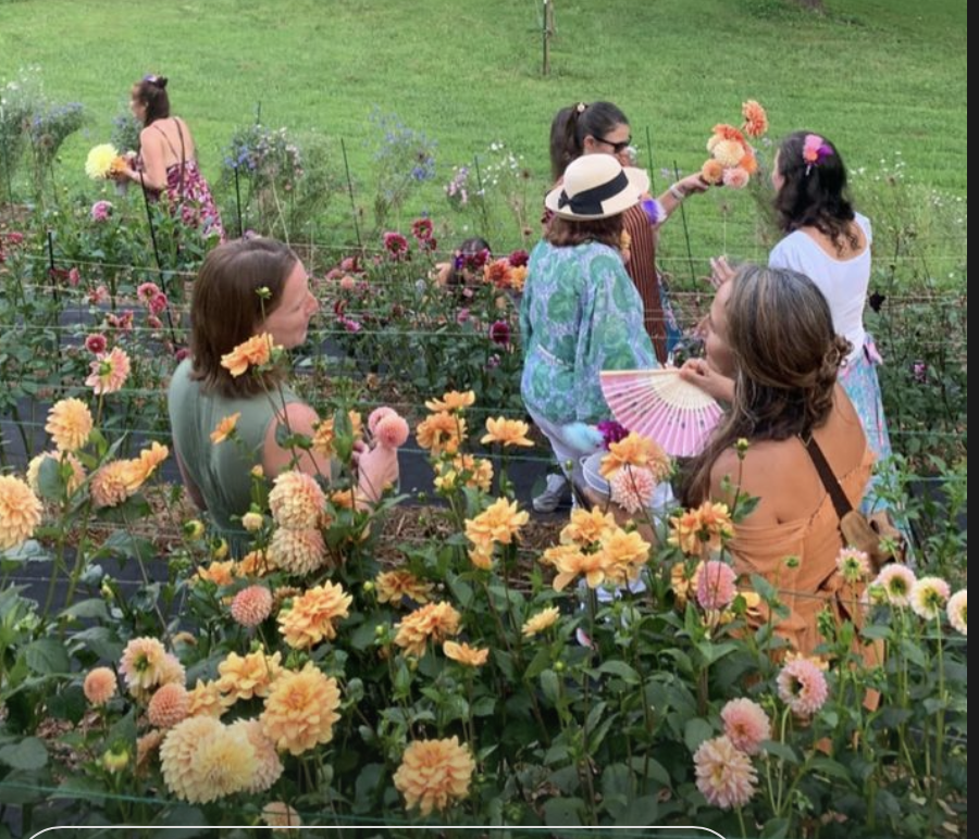 Group of women and children in a flower garden, some holding flowers, with lush green grass in the background.