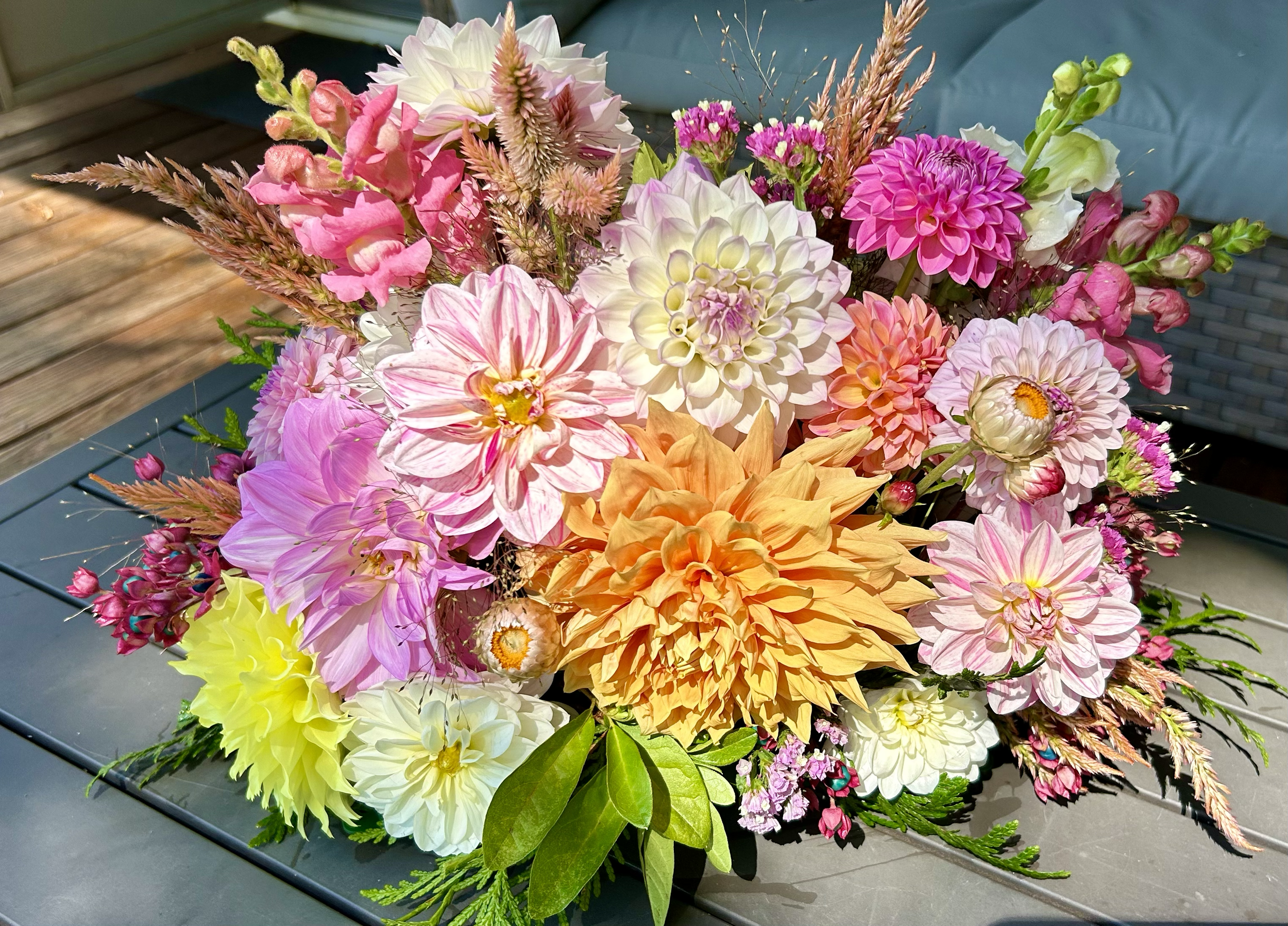 Colorful bouquet of various flowers including dahlias, roses, and other mixed flowers on a gray surface.