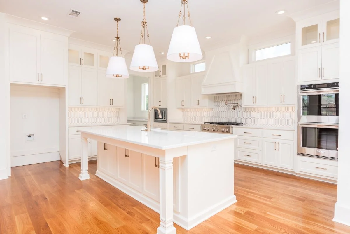 Bright modern kitchen with white cabinets, a center island, hardwood floors, and stainless steel appliances.