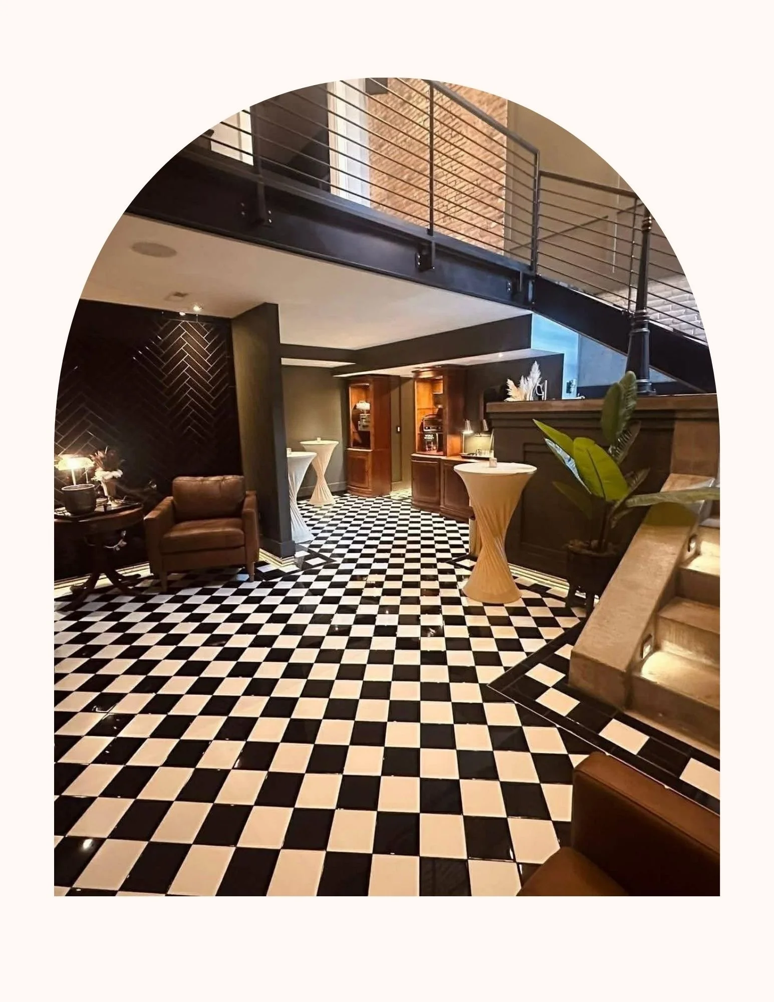 Distinguished Gentlemen's Lounge. Interior of a stylish building featuring a black and white checkered floor, dark wood accents, small tables with lamps, a staircase. Sophisticate space for a groom and groomsmen to get ready for wedding. Fairbury, Il