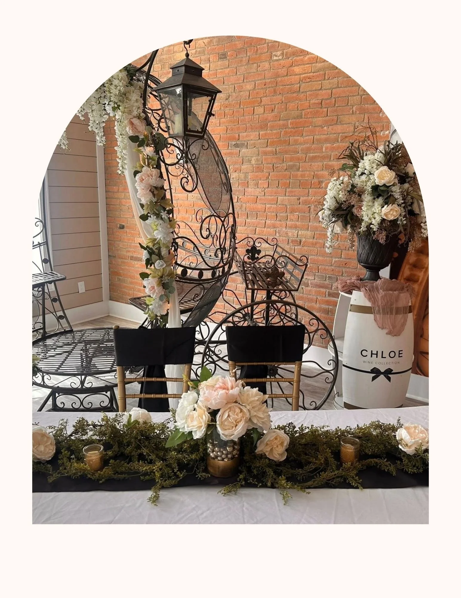 Romantic wedding and event space with decorative wedding or celebration table with white flowers, candles, greenery, against a Cinderella carriage and brick wall background.
