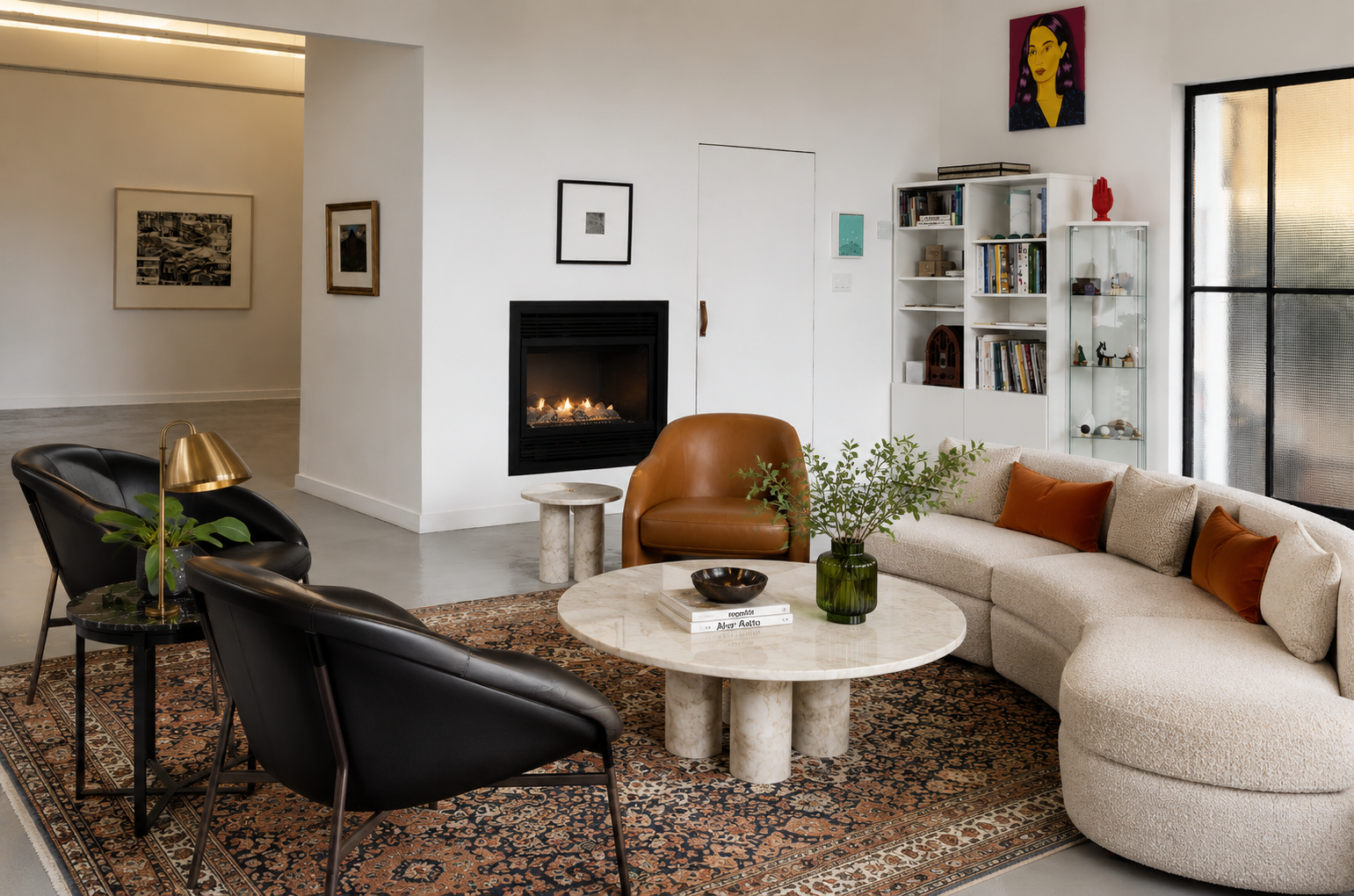 Modern living room with a cream sectional sofa, orange pillows, and a round marble coffee table, black armchairs, a rug, and a white bookshelf near a window with sunlight.