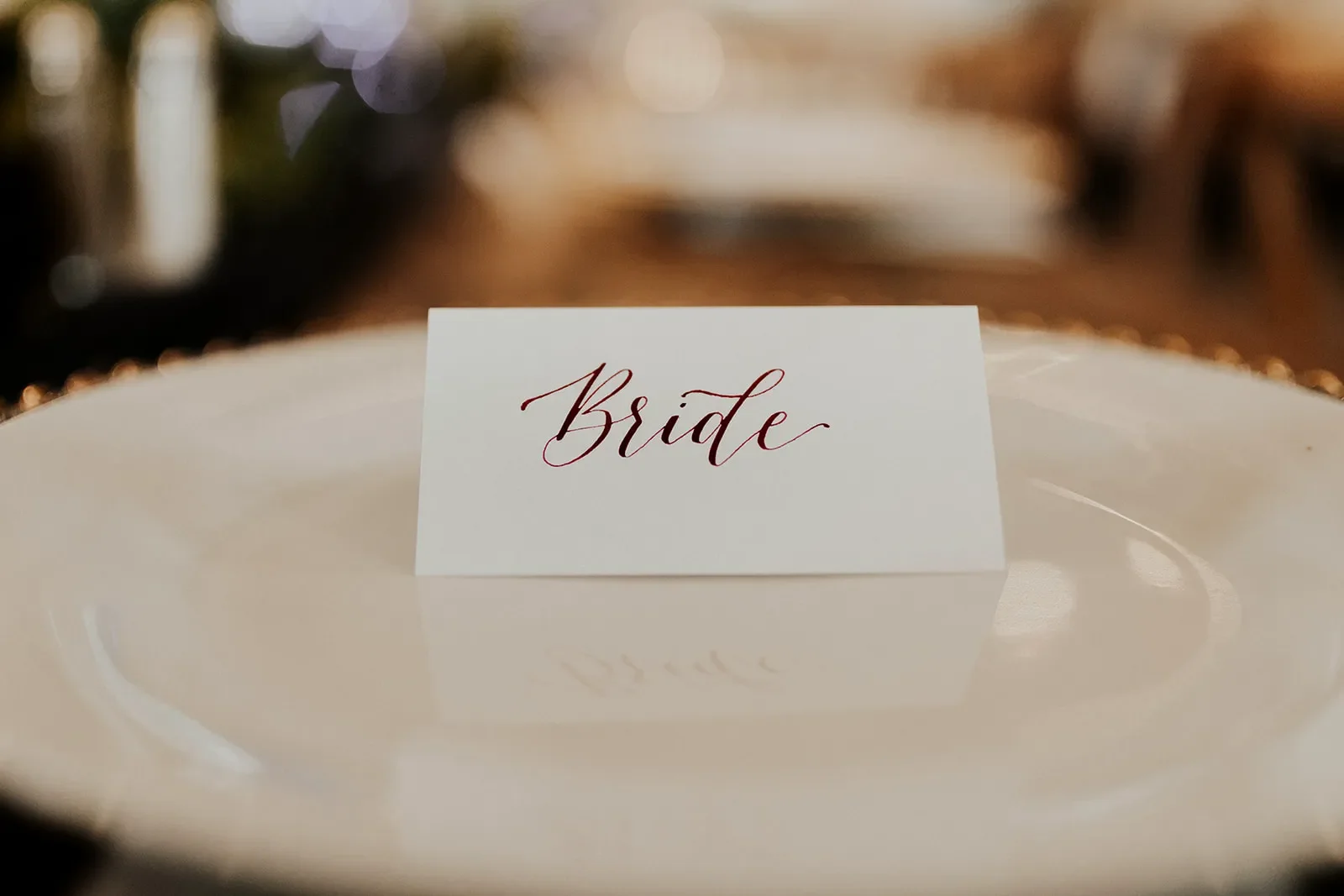 Hand-lettered wedding place card featuring rich marsala ink on a gold-rimmed plate.