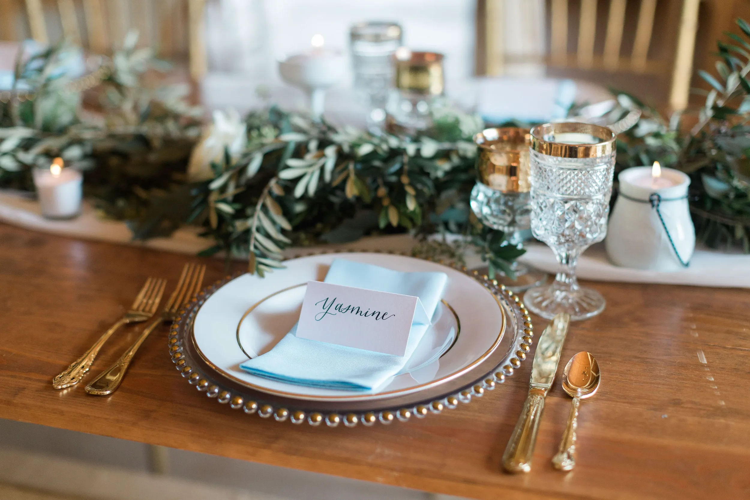It is the fine details that truly welcome your guests. Give your reception tables a personalized, luxurious touch with custom handwritten script place cards. Beautifully paired here with soft blue textiles, elegant gold accents, crystal glassware, an
