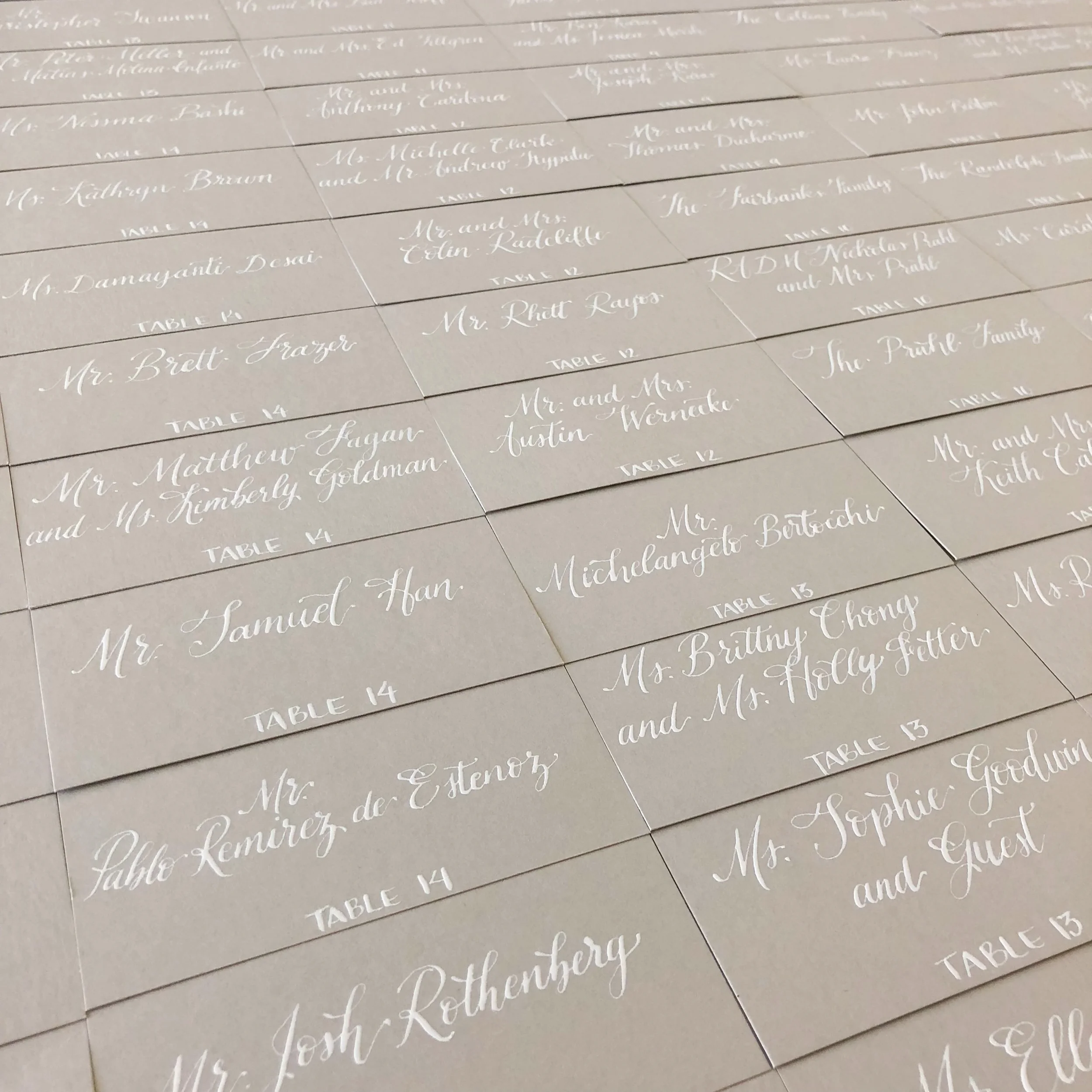 Grey wedding escort cards with white ink calligraphy.