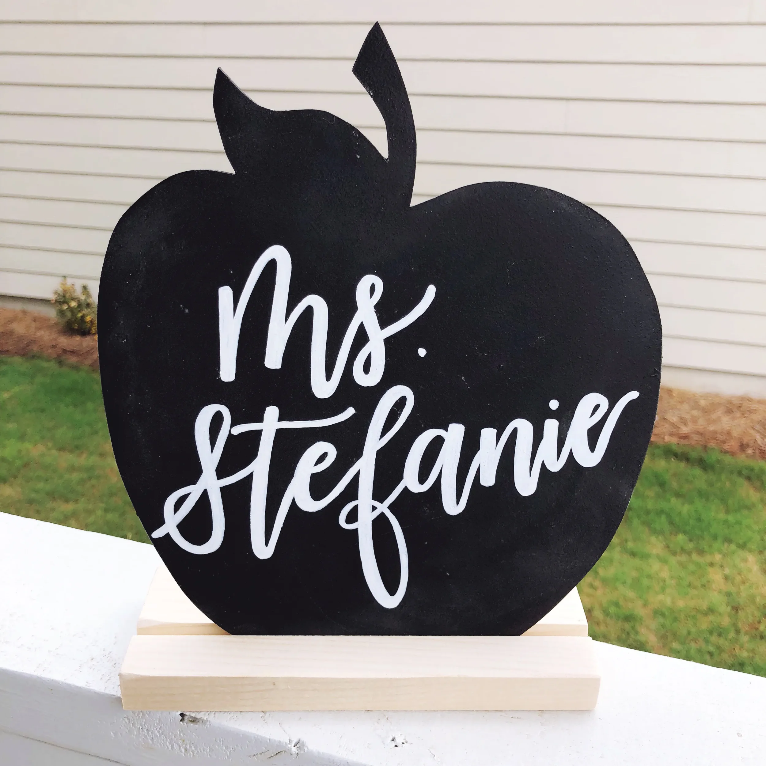 Hand-lettered apple chalkboard sign resting on a wooden block base for a classroom desk.