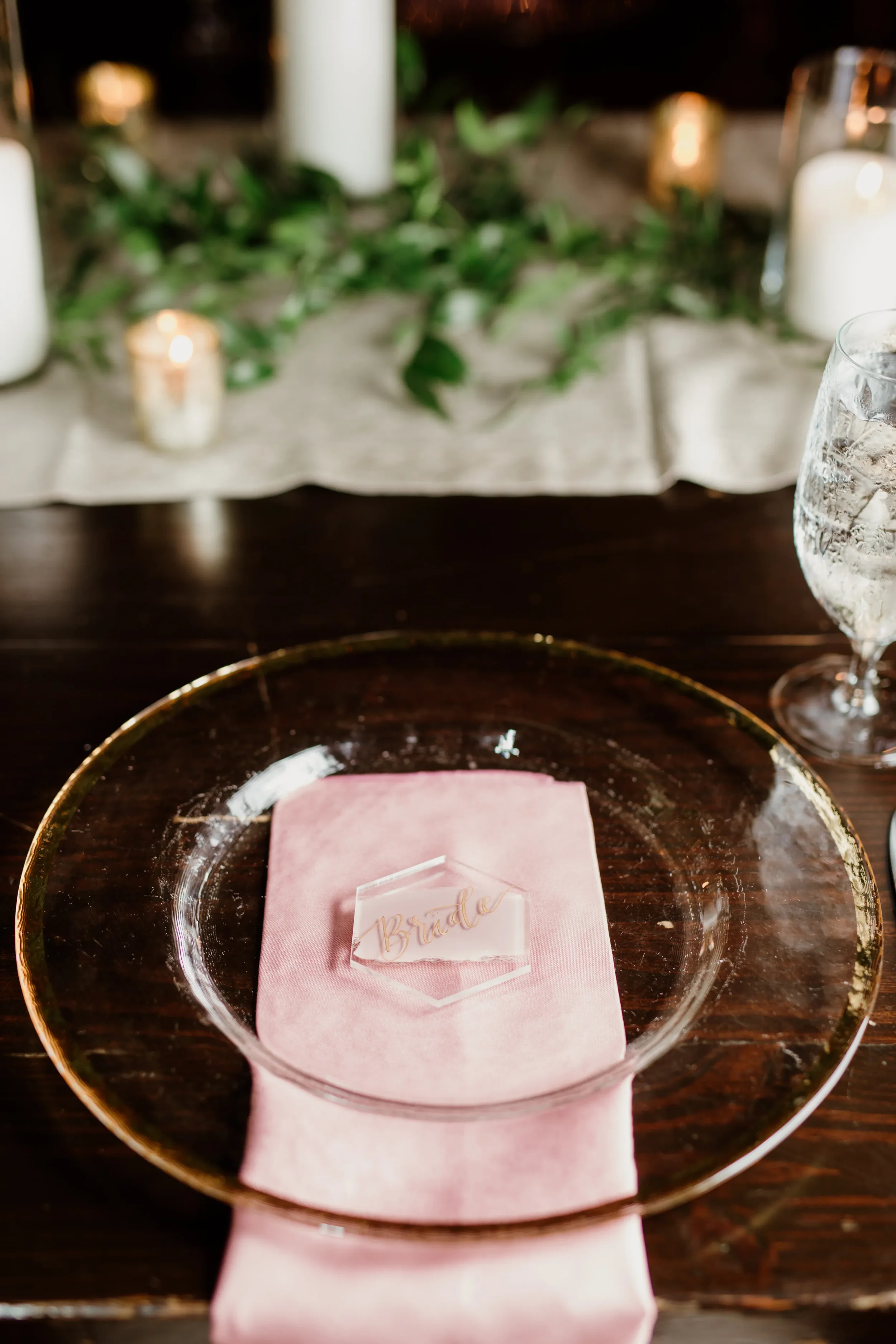 Clear acrylic hexagon place card with gold script calligraphy on a metallic-rimmed plate.