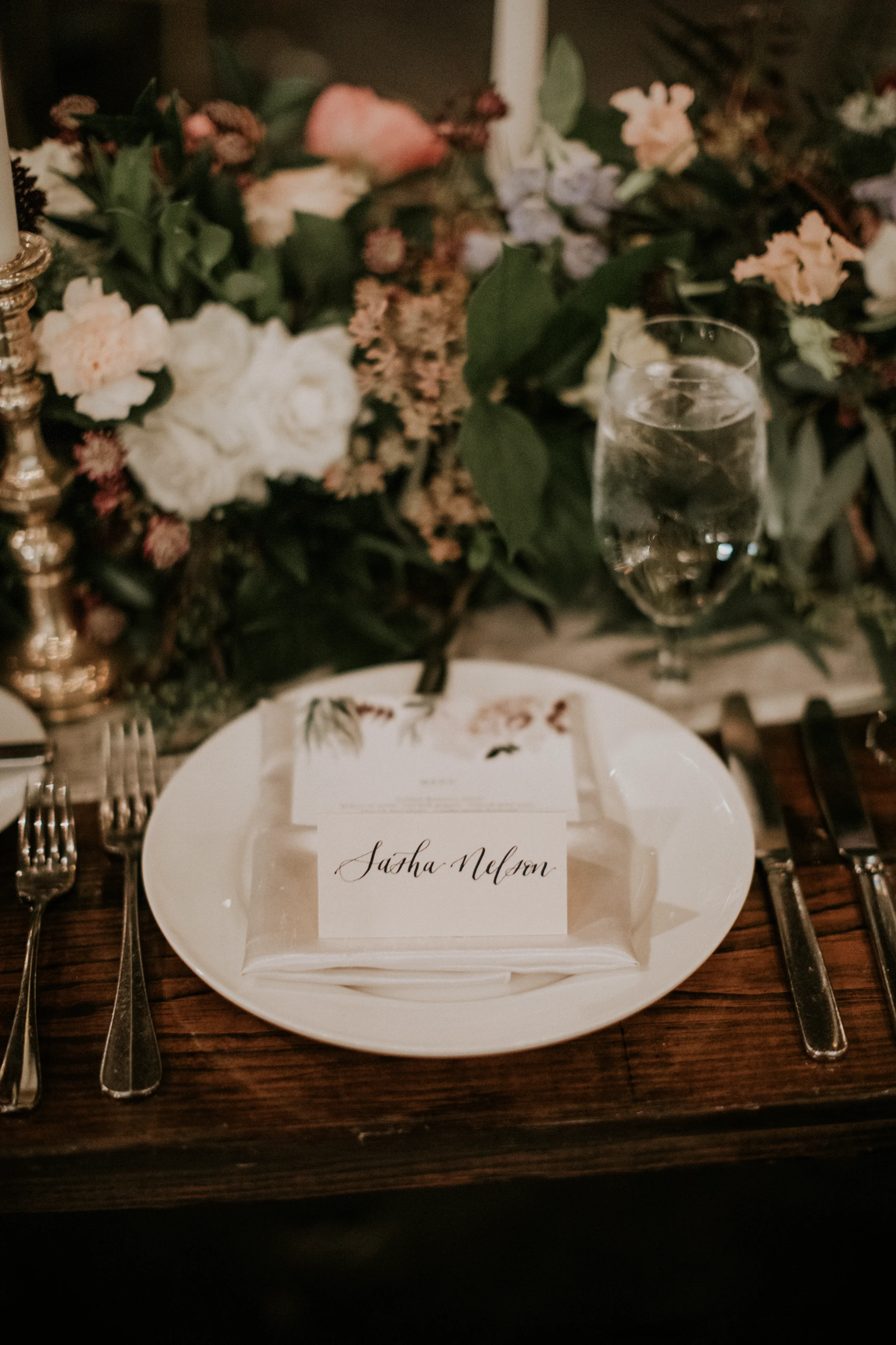 Personalize your wedding reception tablescapes with custom handwritten calligraphy place cards. Paired with elegant floral-accented menus, romantic brass candlesticks, and organic garden centerpieces, fine script paper goods create an unforgettable, 