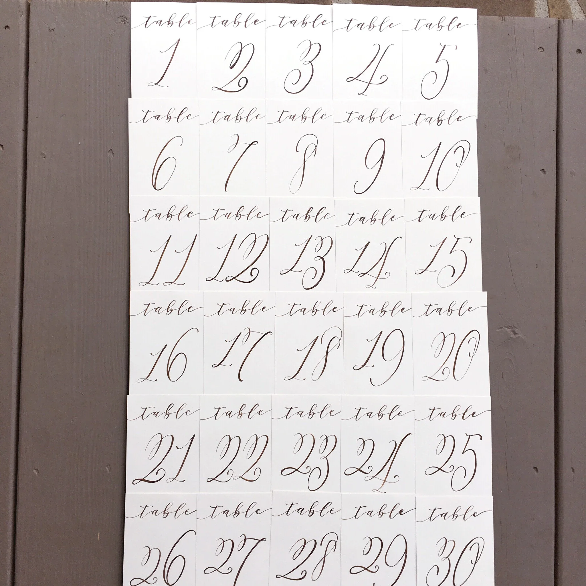 Ensure seamless reception navigation with clear, elegant script table numbers. Styled with a classic numeral paired with delicate handwritten text above, this uniform paper collection offers timeless legibility for large wedding receptions.