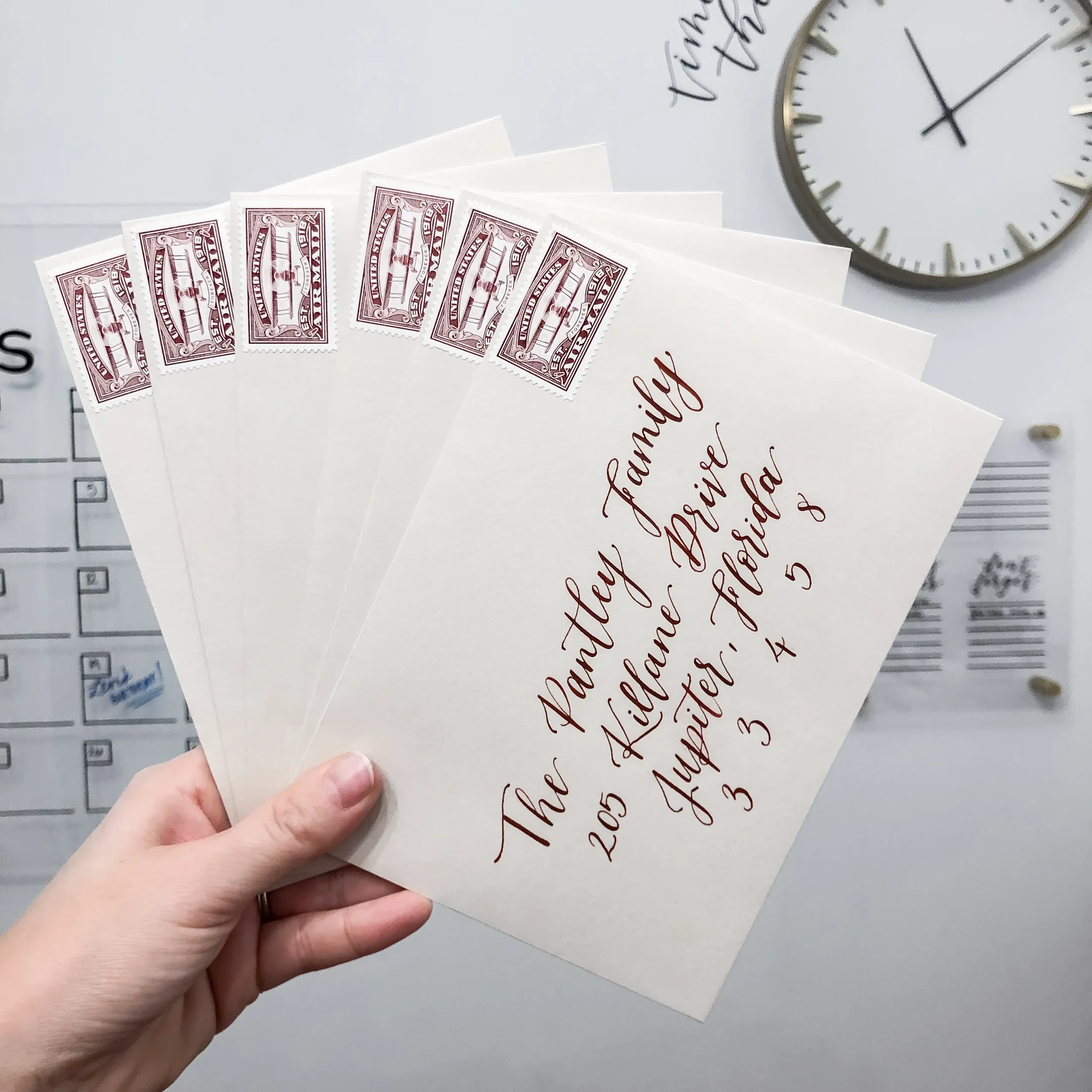 Taupe kraft paper envelopes addressed in a deep burgundy calligraphy font with vintage stamps for fall or winter weddings.