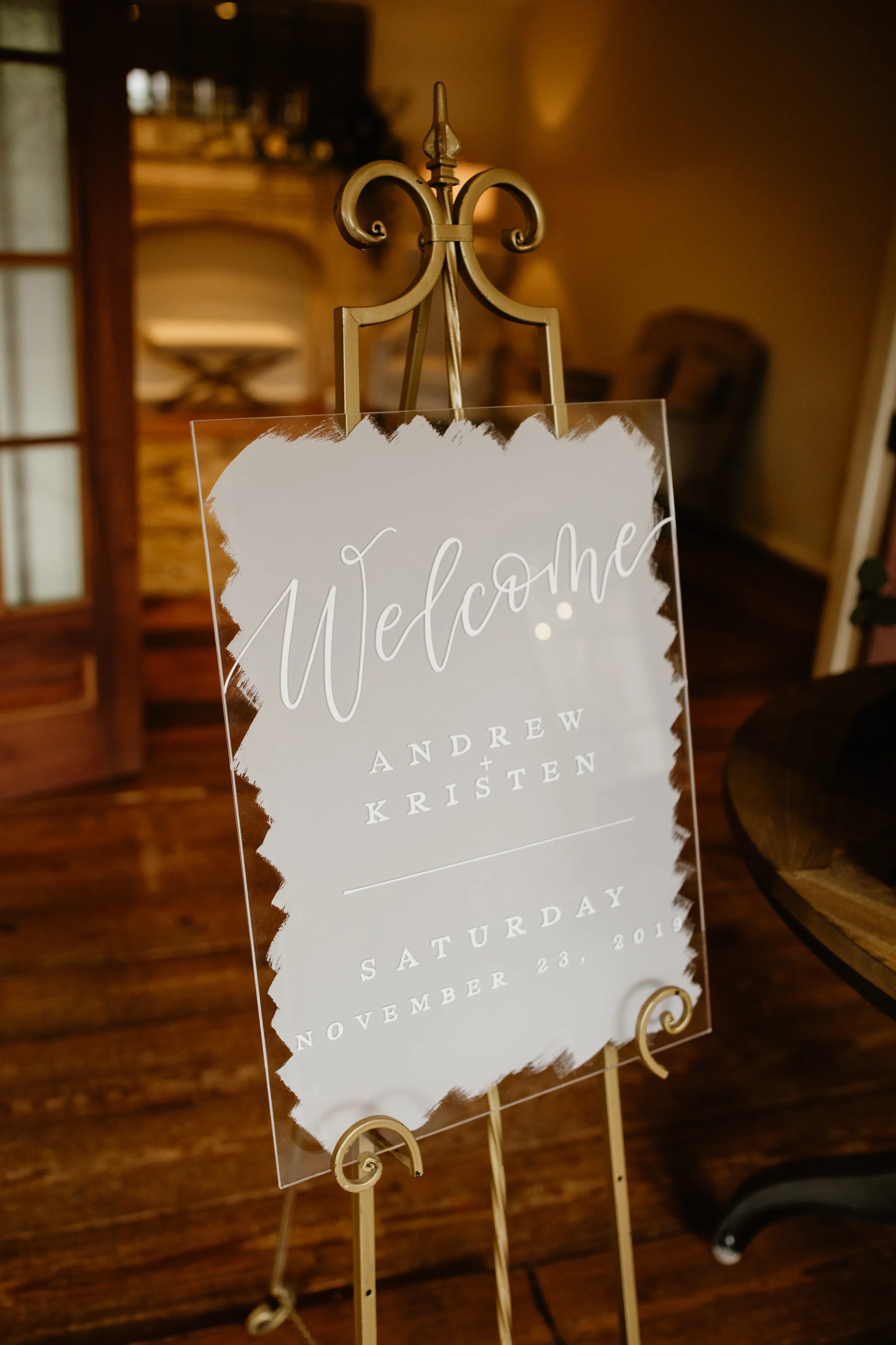 Large painted-back acrylic wedding welcome sign with white ink calligraphy on a gold easel.
