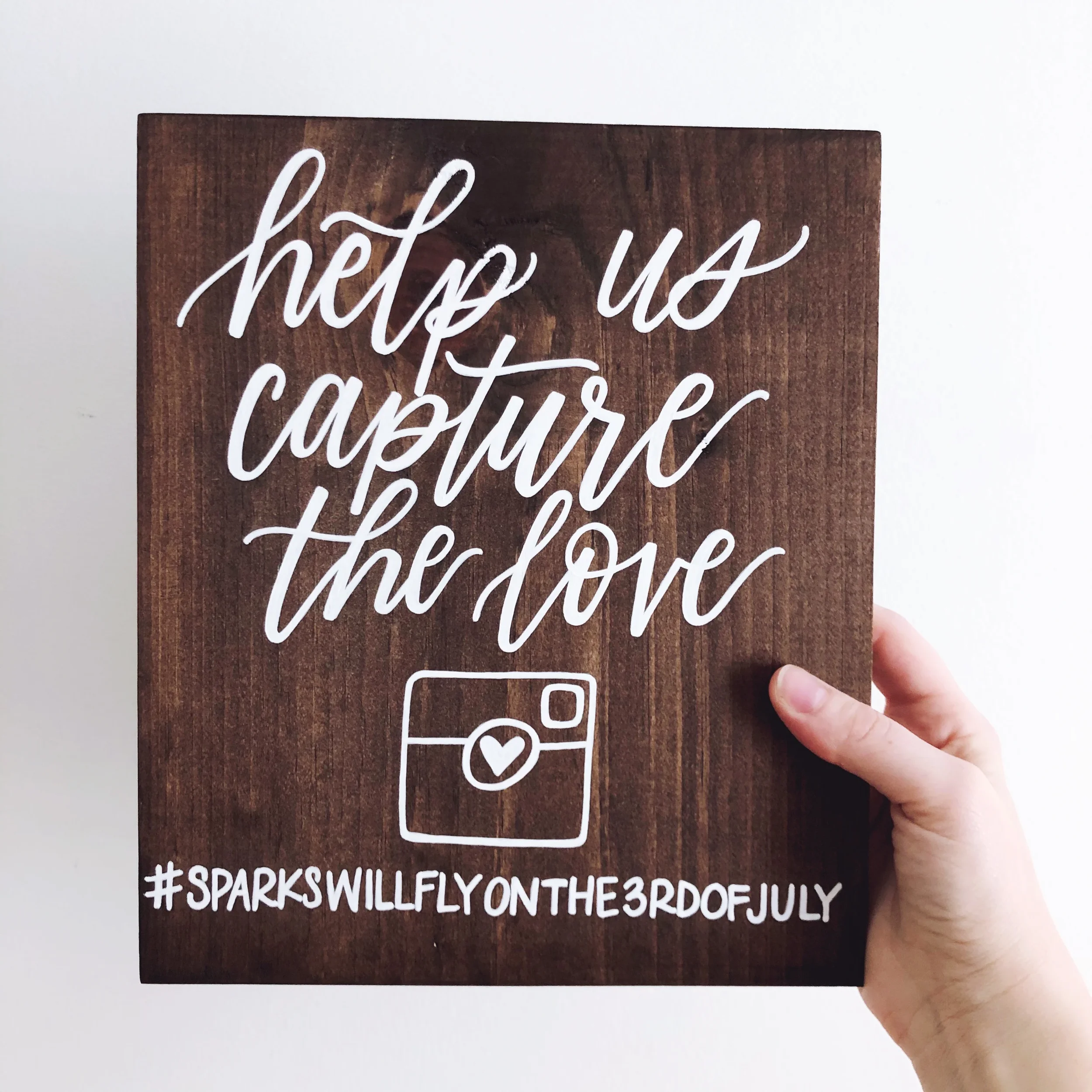 Custom stained wood wedding hashtag sign written in white hand-lettering script.