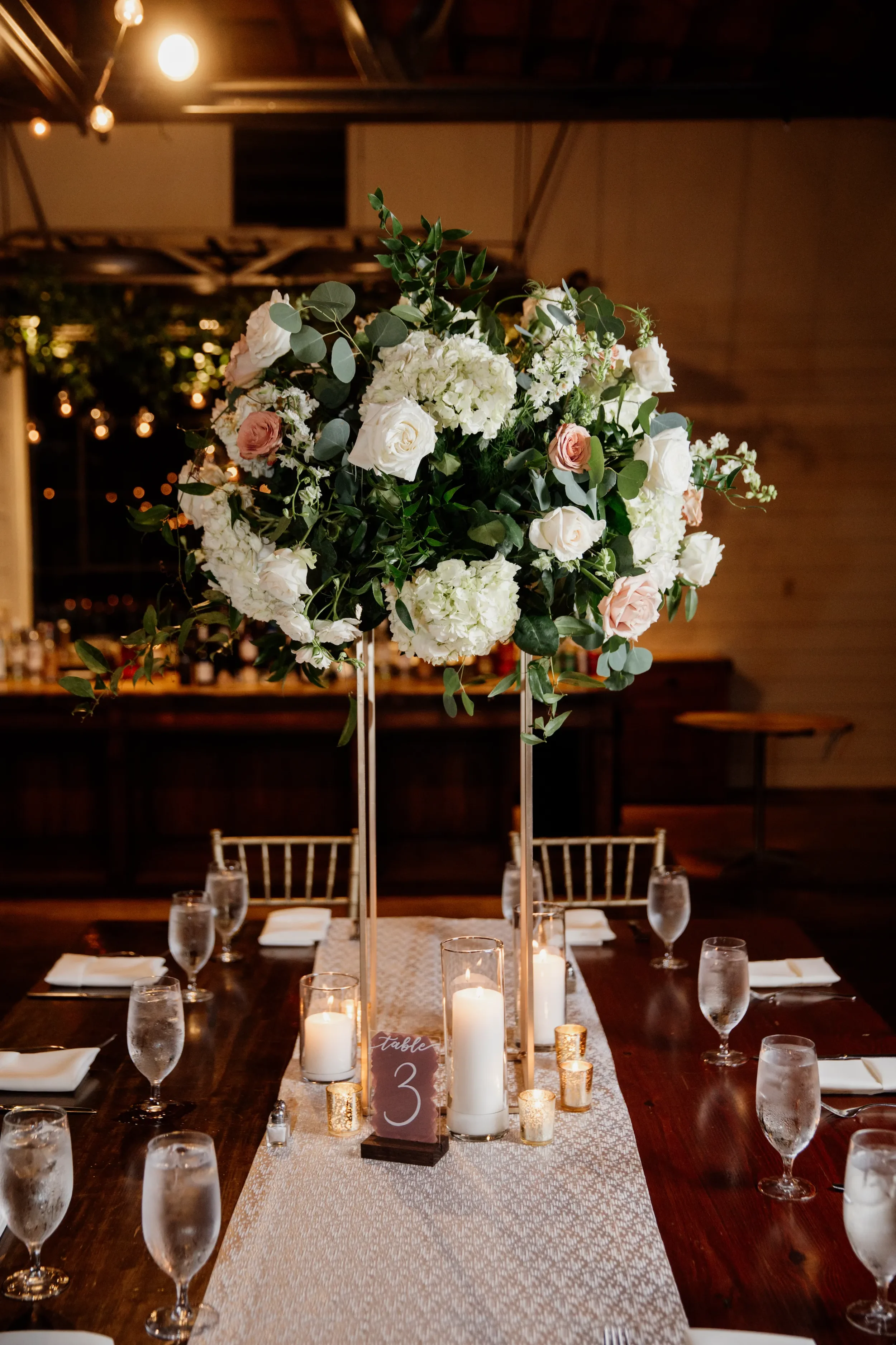 Modern wedding acrylic table numbers. Featuring a rich, dusty mauve painted back and crisp white hand-lettered numbers, this signage design sits in a dark wooden block to beautifully complement romantic lush floral centerpieces and glowing candleligh