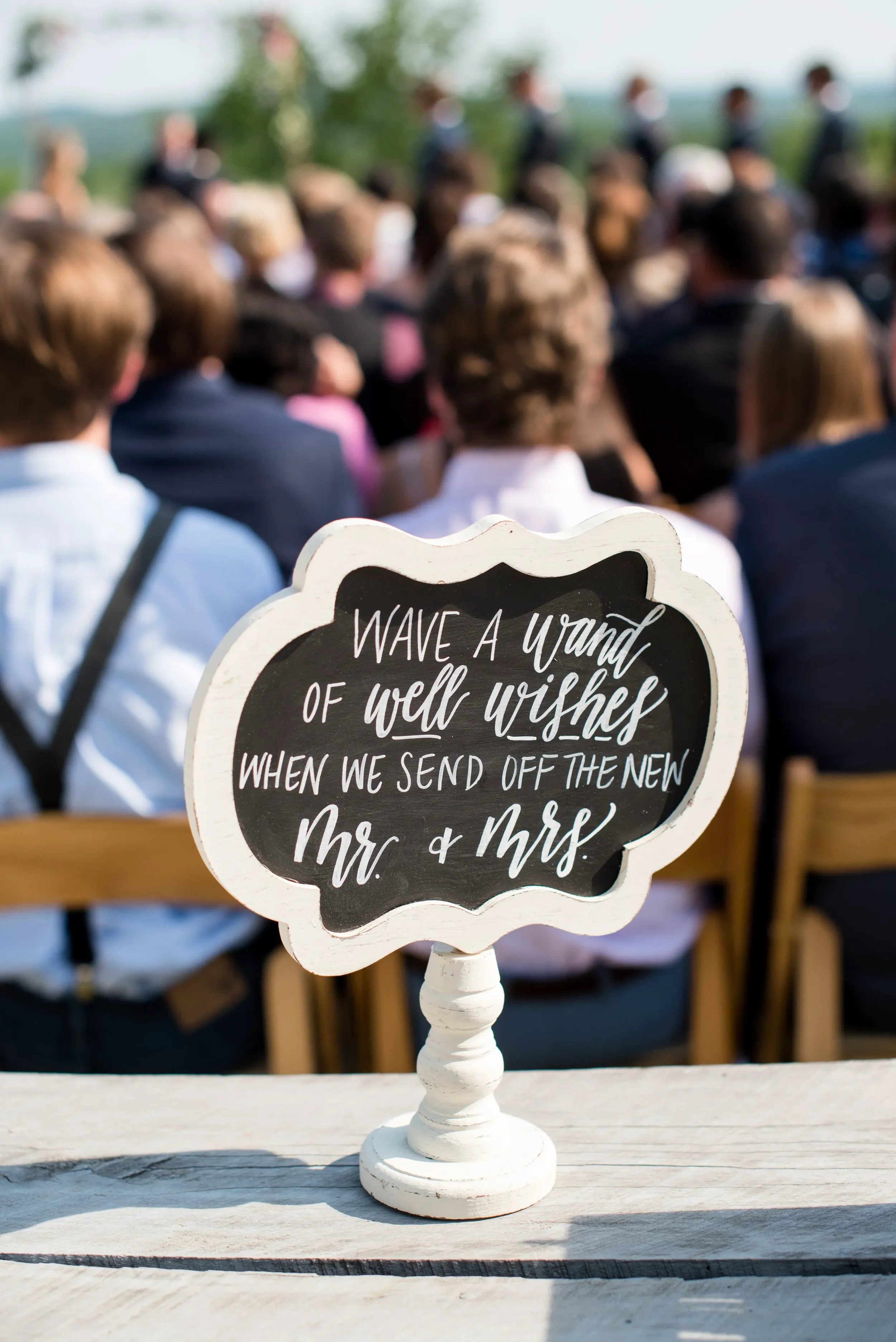 Mini chalkboard sign with white script calligraphy prompting guests to give well wishes to the newlyweds.