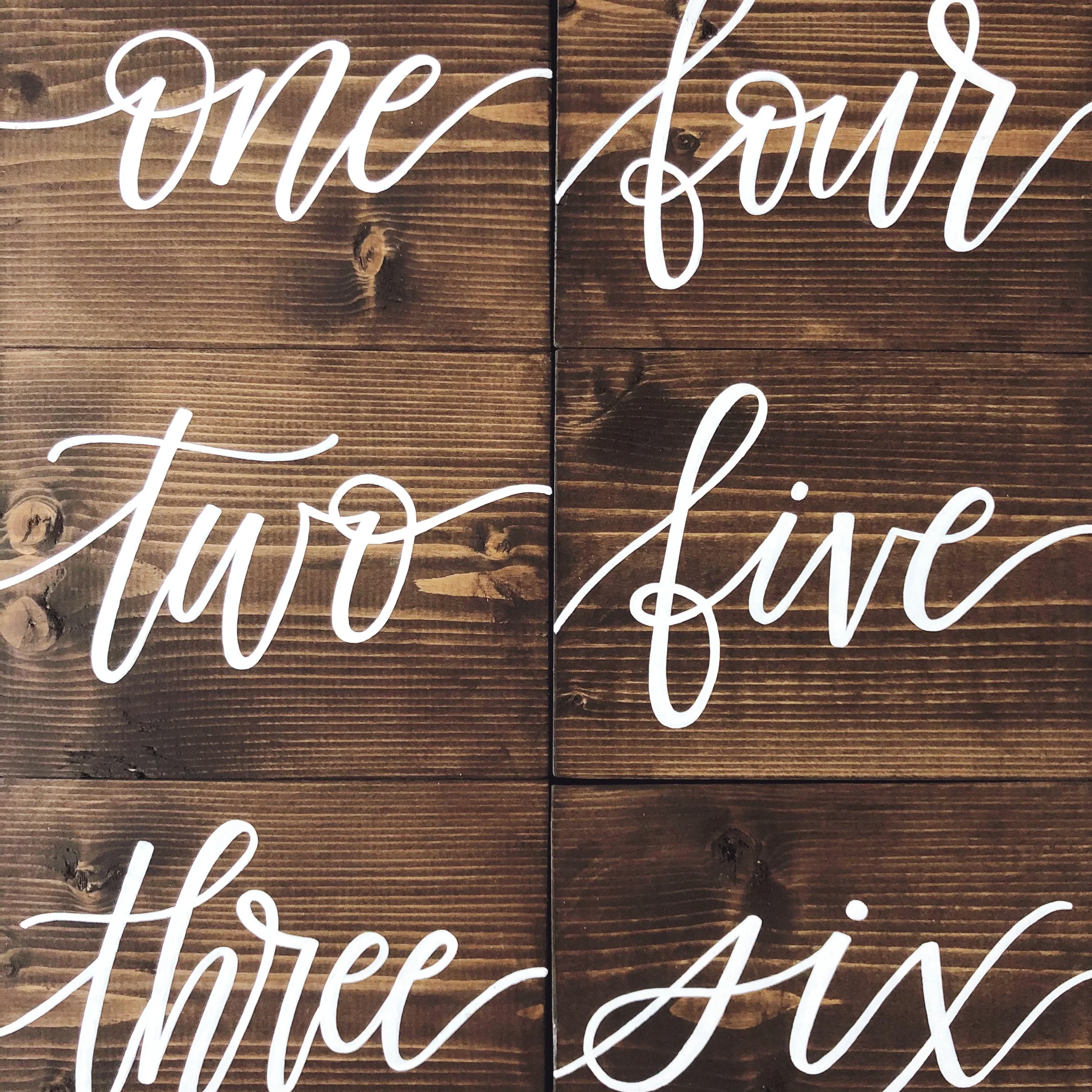 Dark brown stained wood block table numbers written in white script.