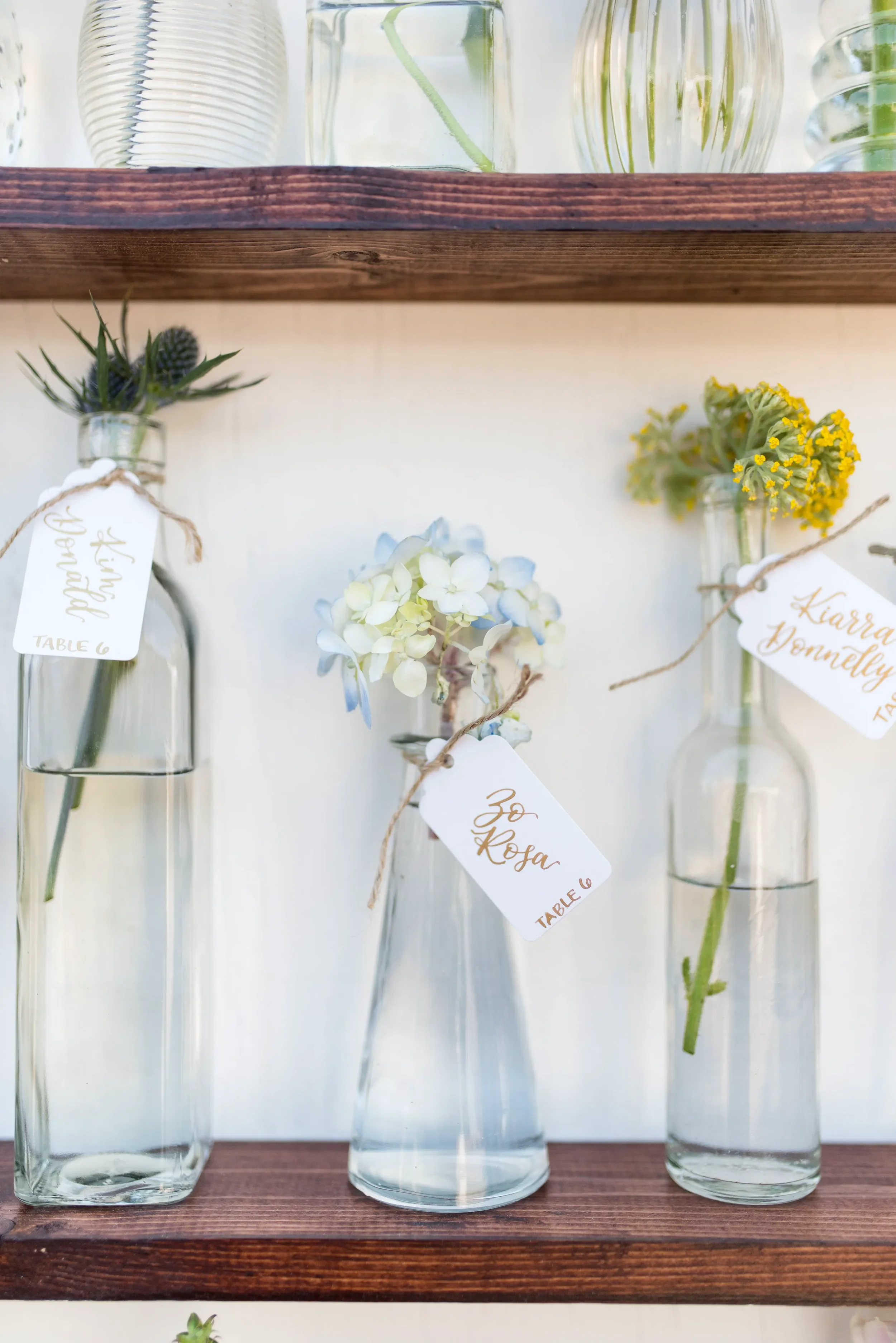 Whimsical garden wedding escort card display with clear glass bud vases and hand-lettered tags.