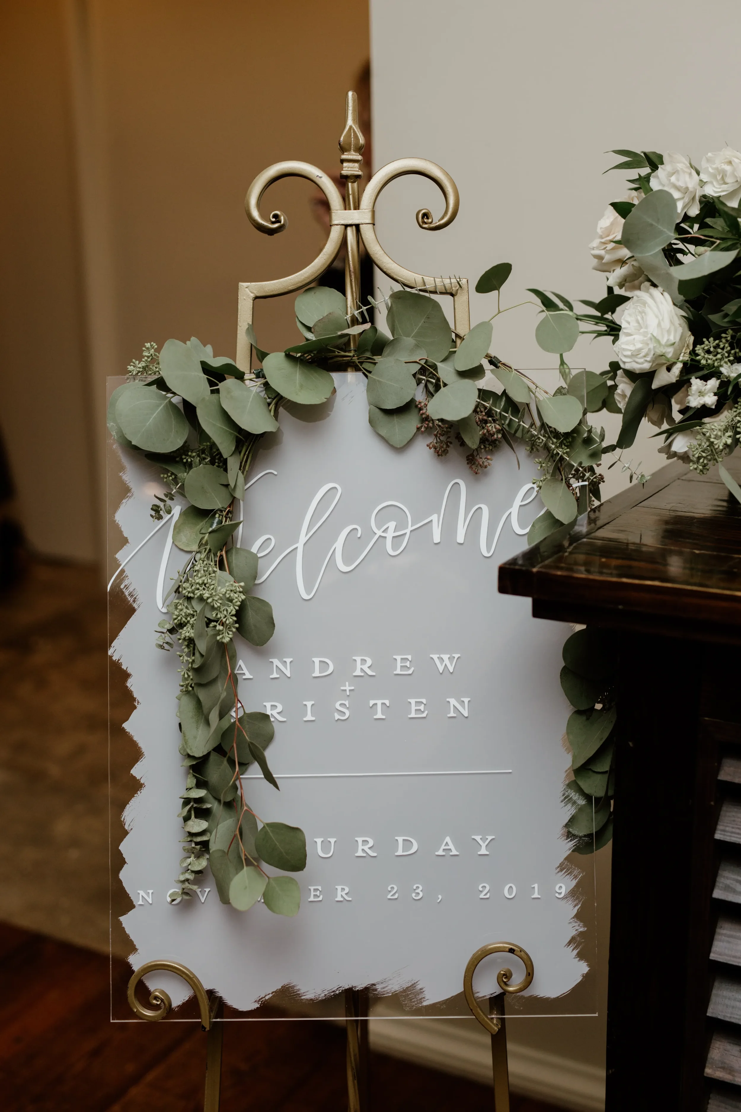 Make a stunning first impression at your venue with an oversized clear acrylic wedding welcome sign. Featuring a custom textured white painted-back brushstroke finish and elegant white script calligraphy, it stands gracefully on an ornate vintage gol