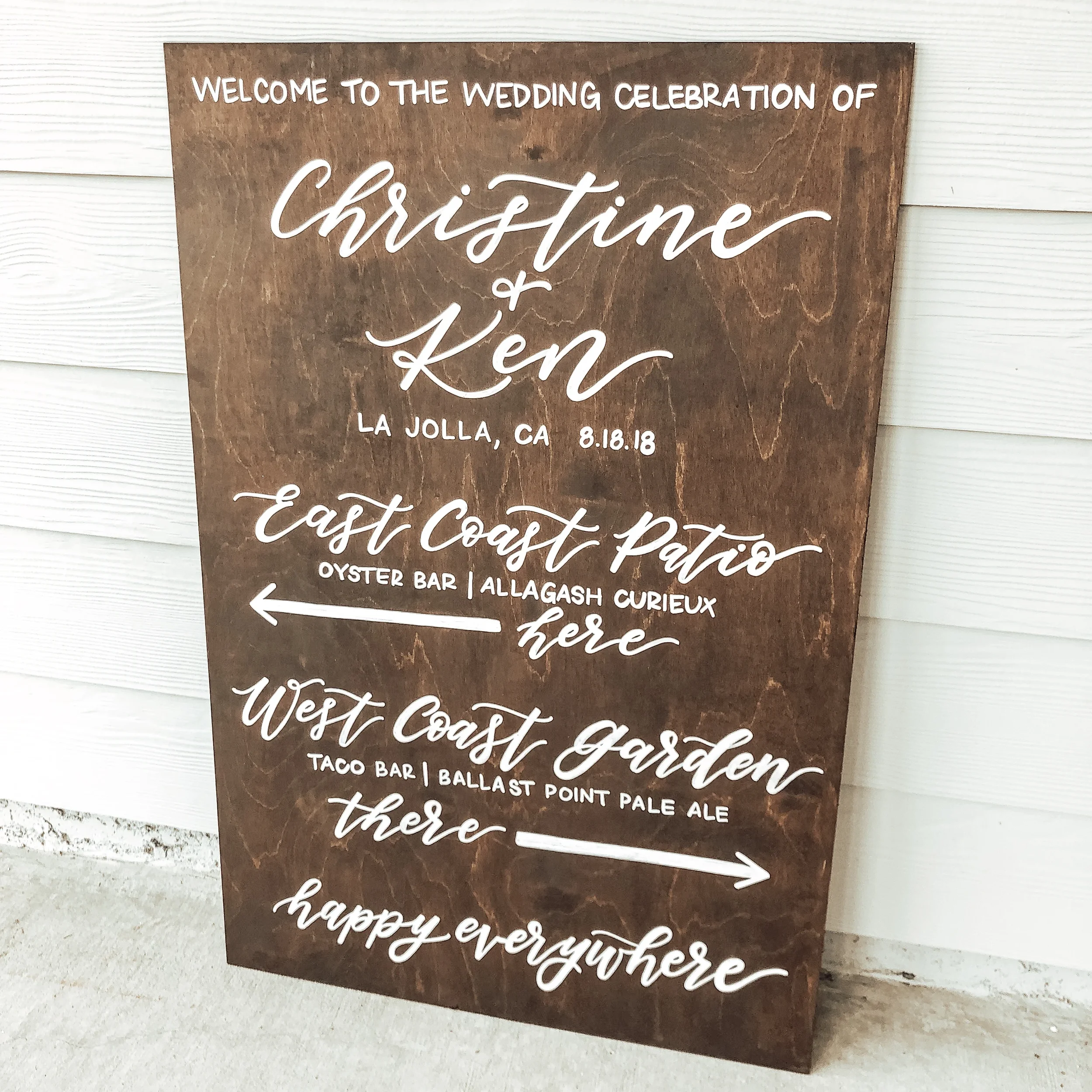 Large dark wood sign welcoming guests to Christine and Ken's wedding with directional arrows to the oyster bar and garden.