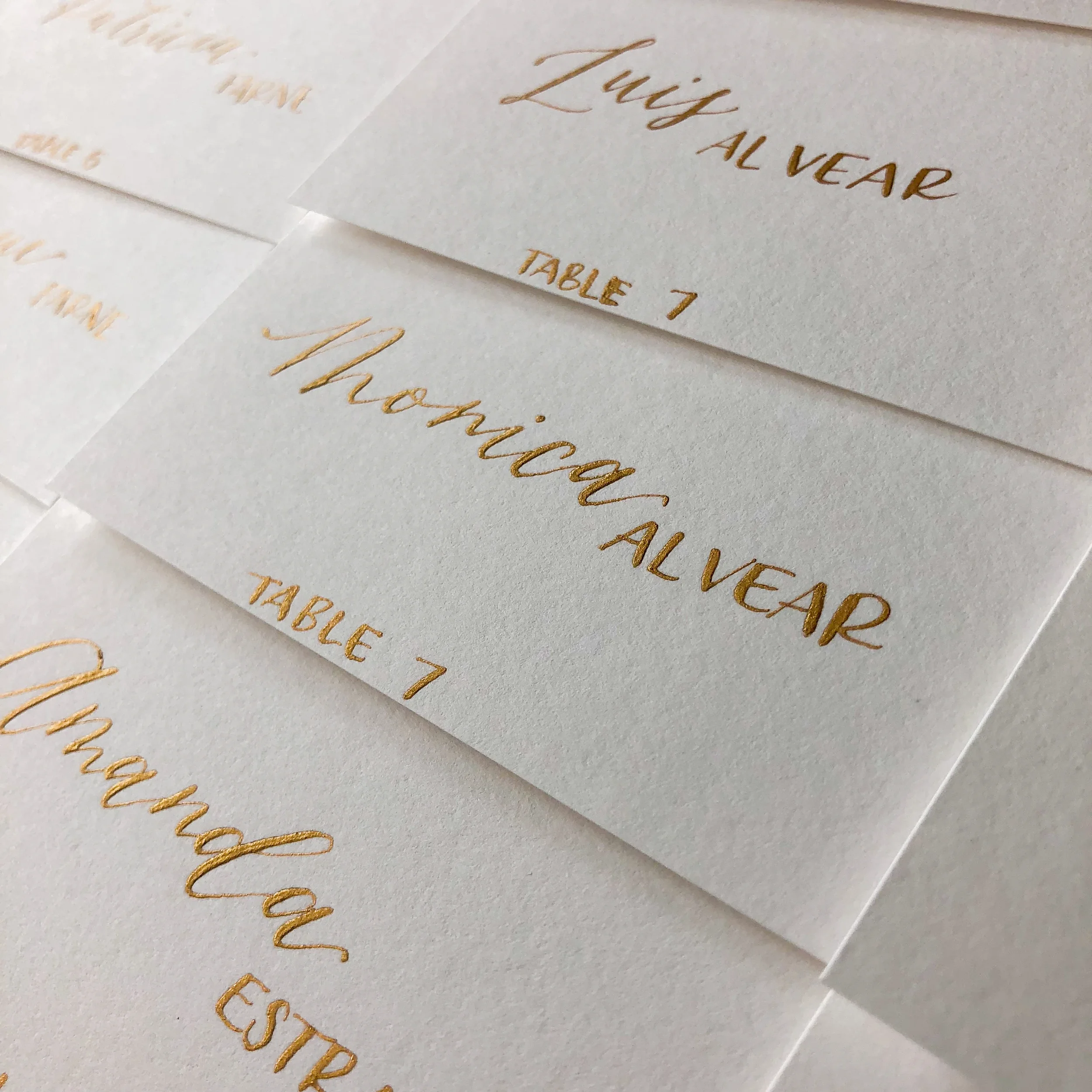 White cardstock paper escort cards with gold ink mixed font calligraphy.
