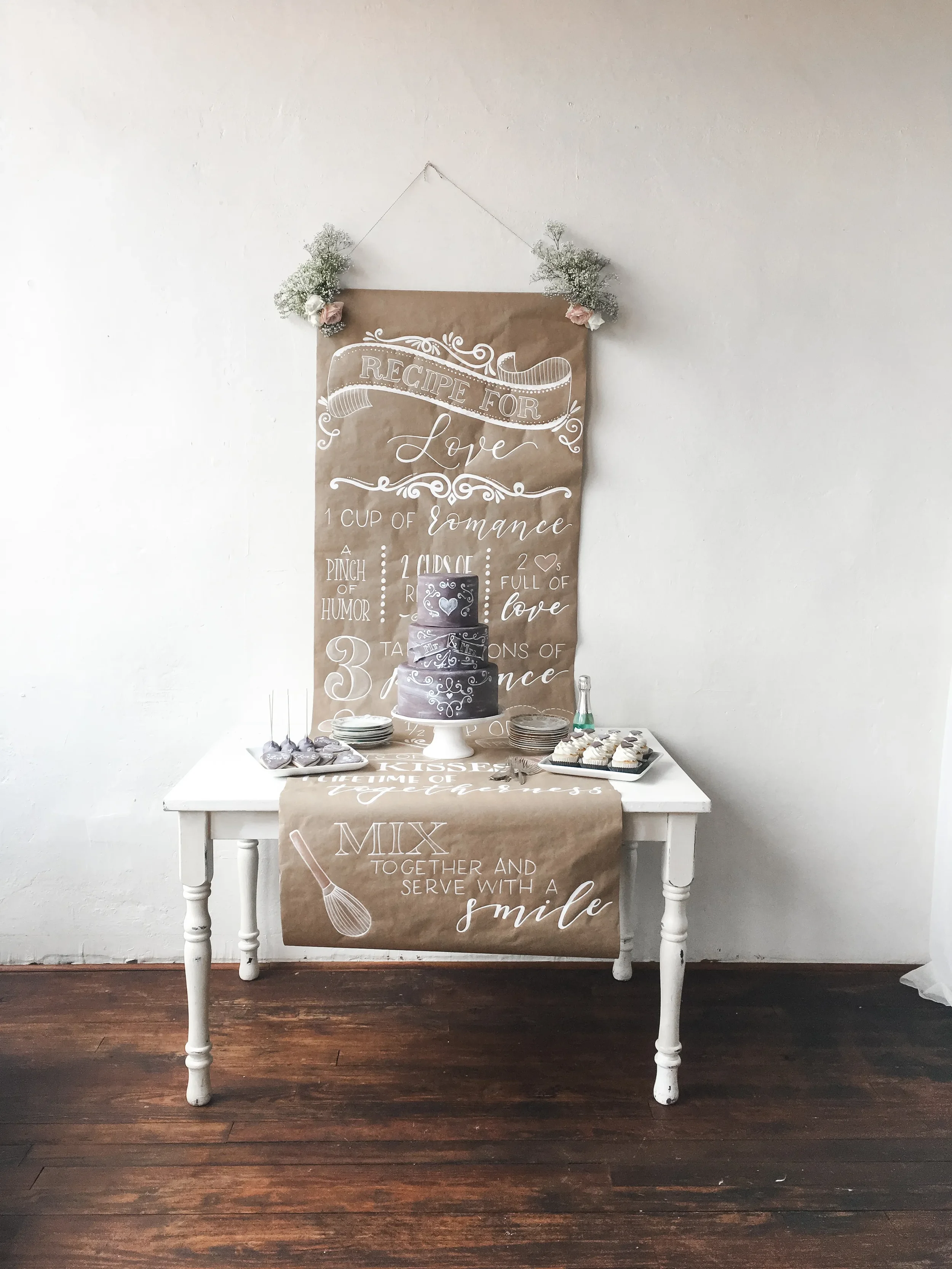 Rustic calligraphy on a long brown paper backdrop banner behind a tiered wedding cake.