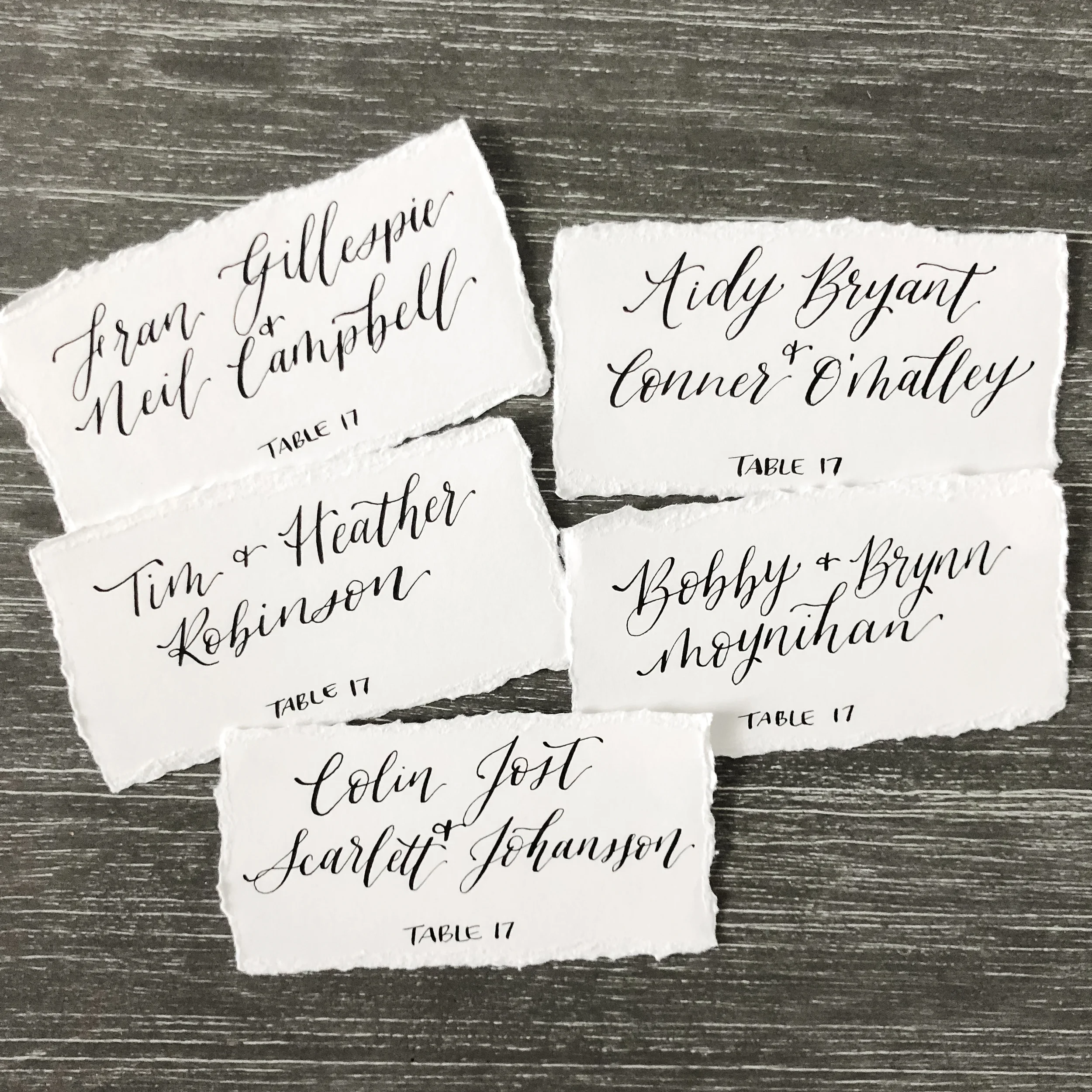 Deckled edge white paper wedding escort cards with classic black calligraphy.