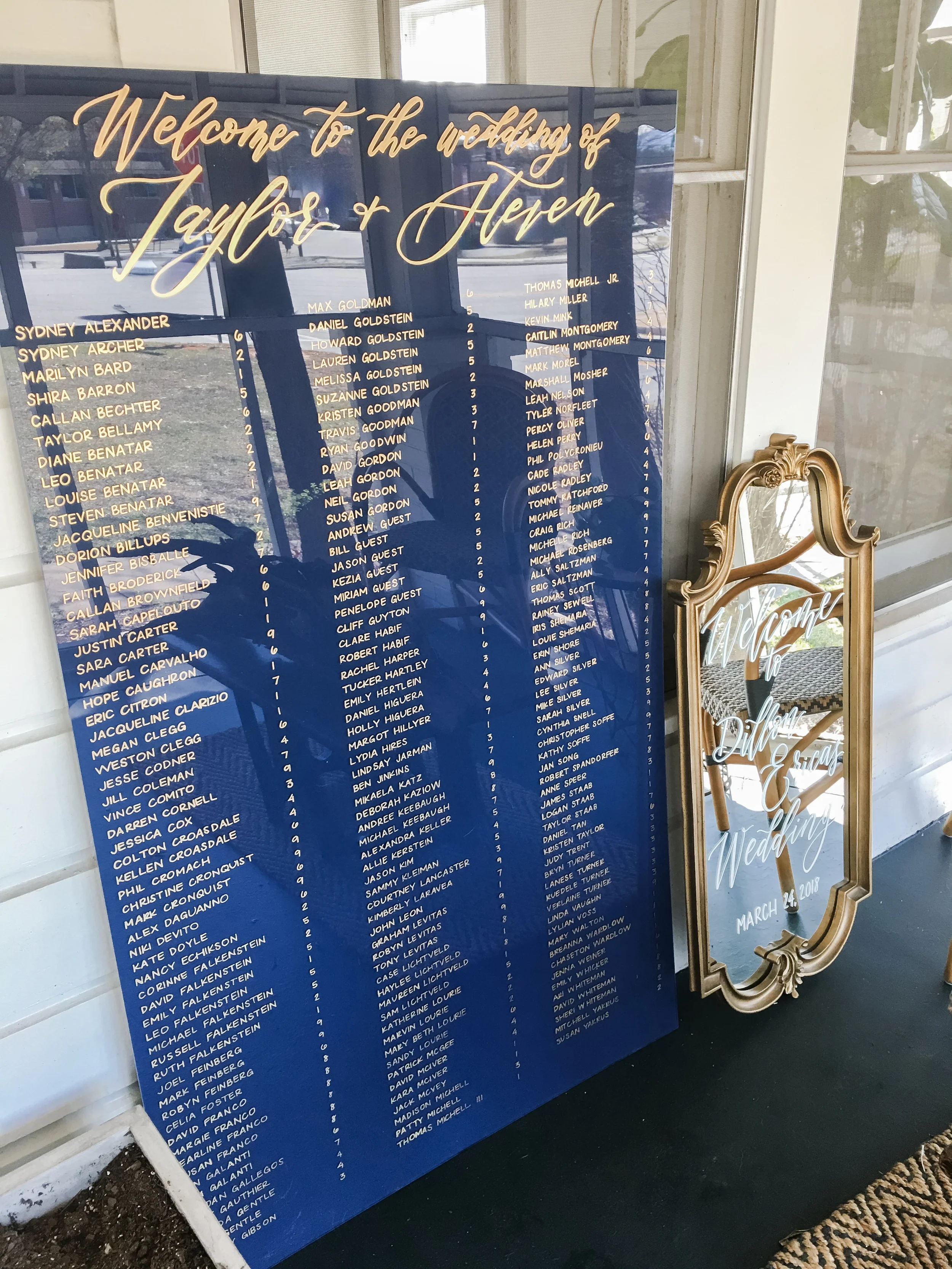 Large navy blue painted-back acrylic wedding seating chart with gold hand-lettering